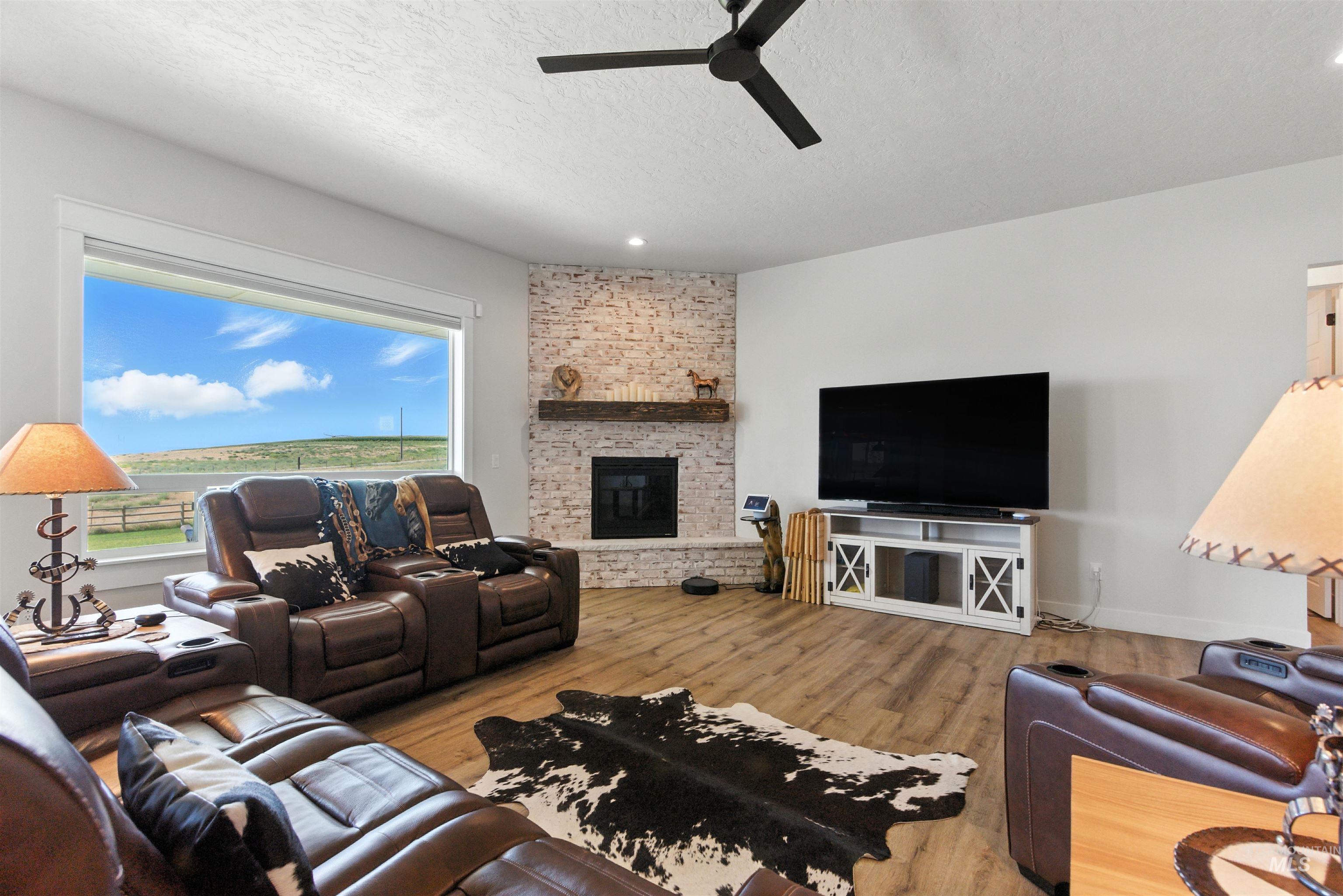 Living area with a stone fireplace, a textured ceiling, wood finished floors, and a ceiling fan