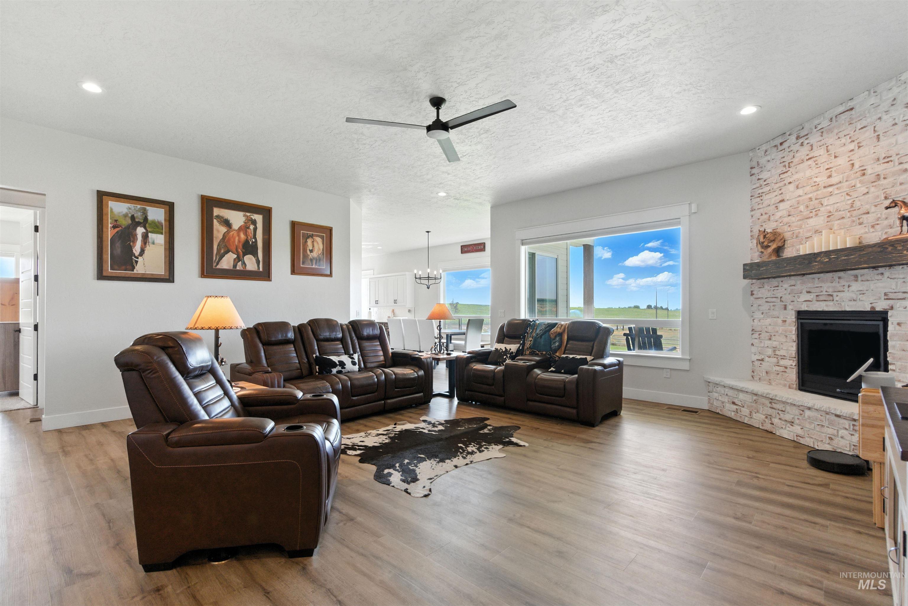 Living room with a fireplace, ceiling fan, wood finished floors, a chandelier, and a textured ceiling