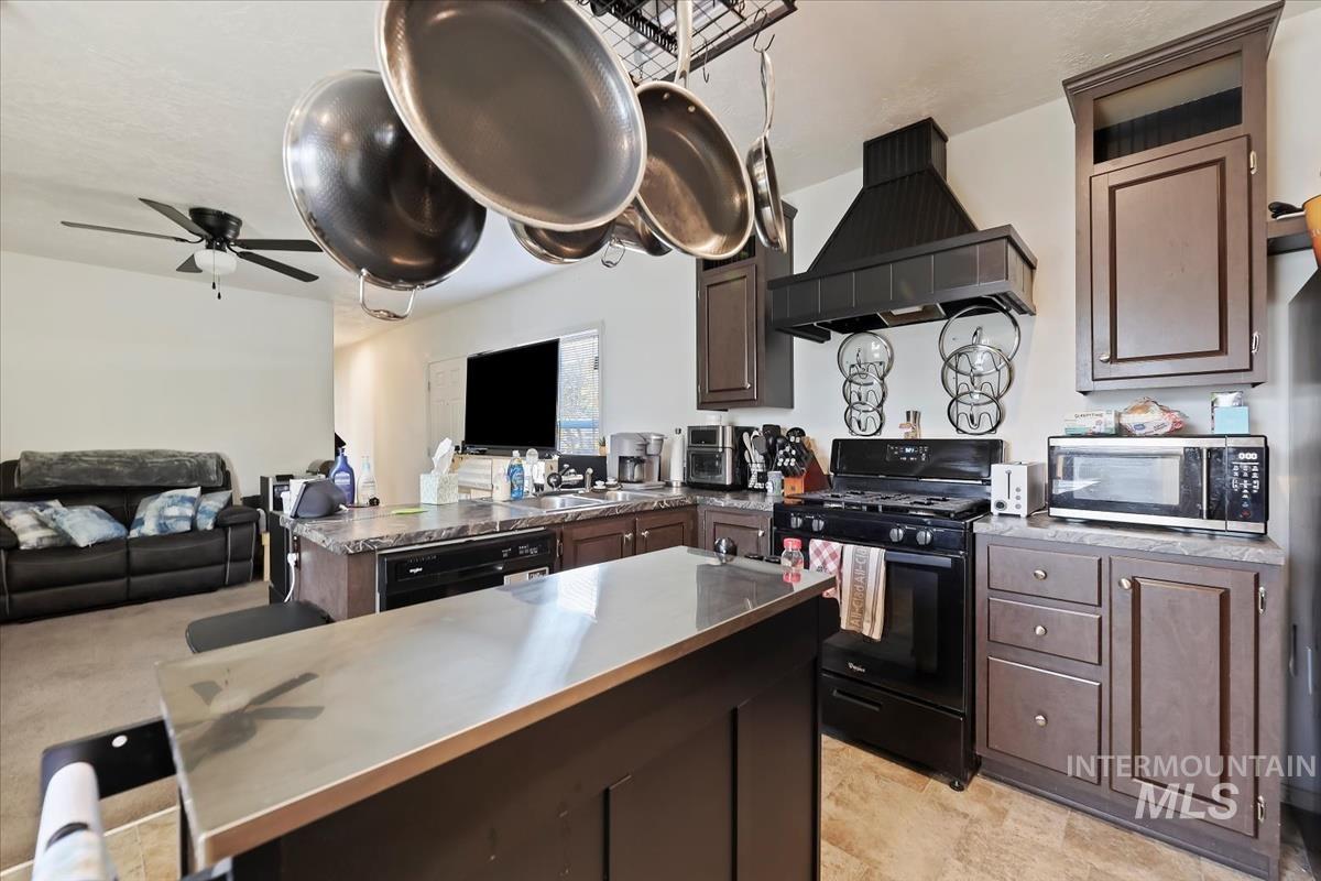 Kitchen with open floor plan, black appliances, exhaust hood, dark brown cabinetry, and a peninsula