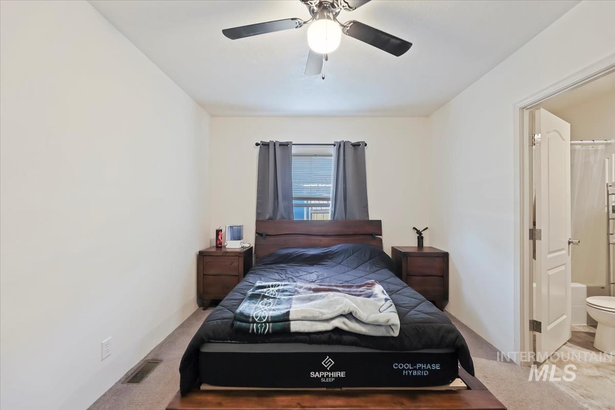 Carpeted bedroom with ensuite bath and a ceiling fan