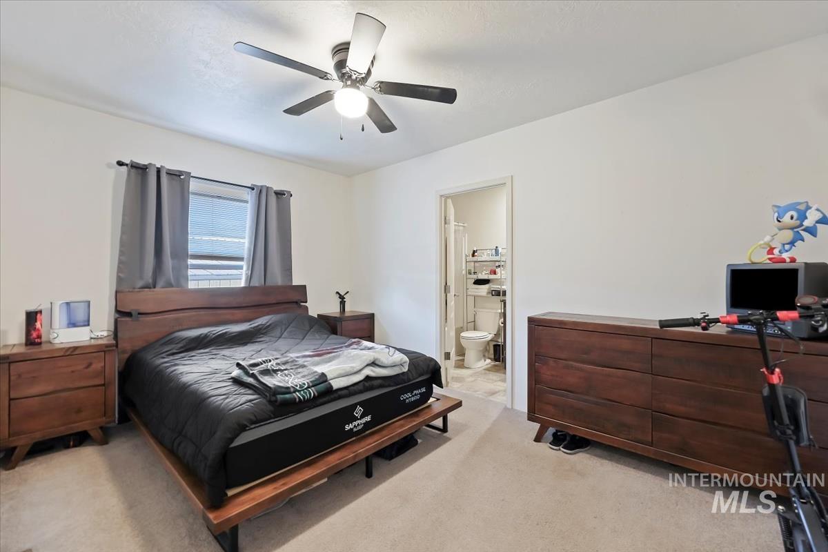 Bedroom featuring light carpet, ceiling fan, ensuite bath, and a desk