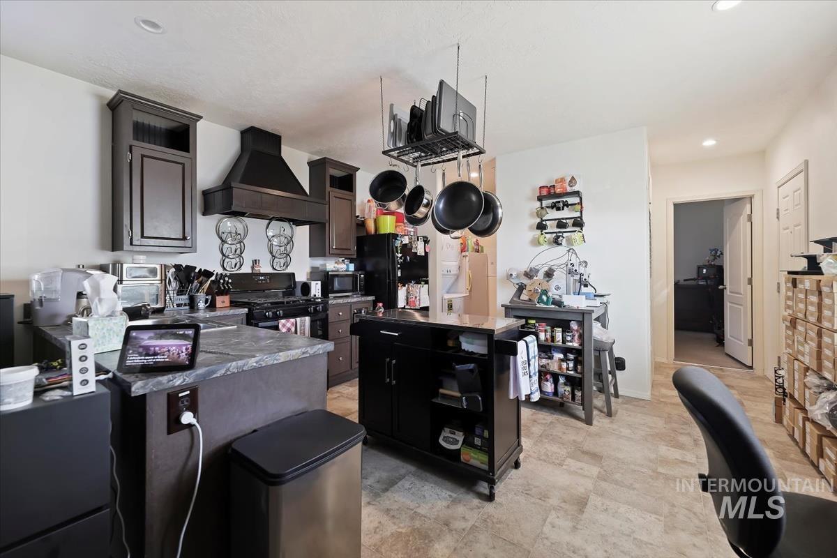 Kitchen with premium range hood, a peninsula, recessed lighting, dark countertops, and a center island