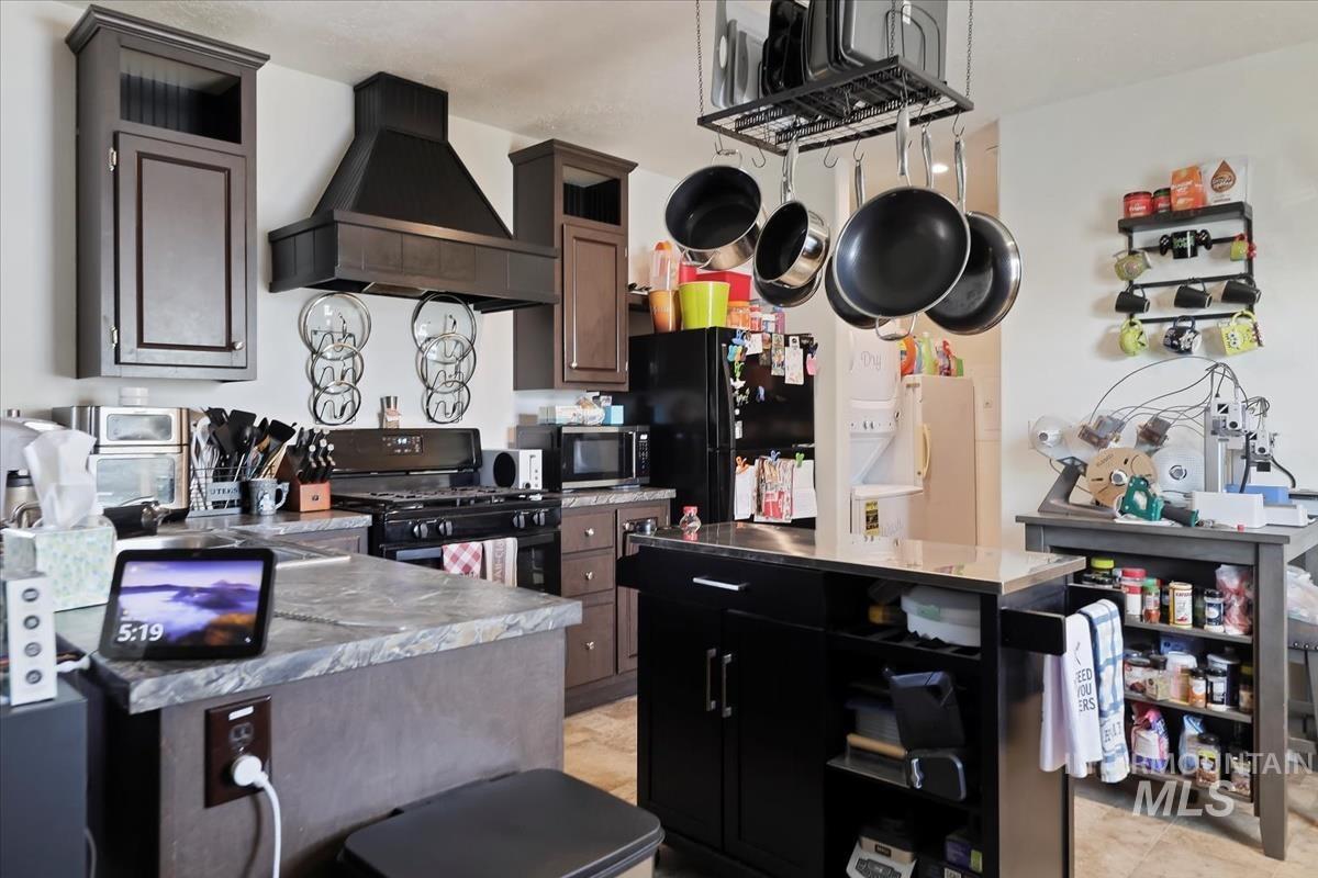 Kitchen with open shelves, wall chimney exhaust hood, black appliances, dark cabinetry, and dark brown cabinets