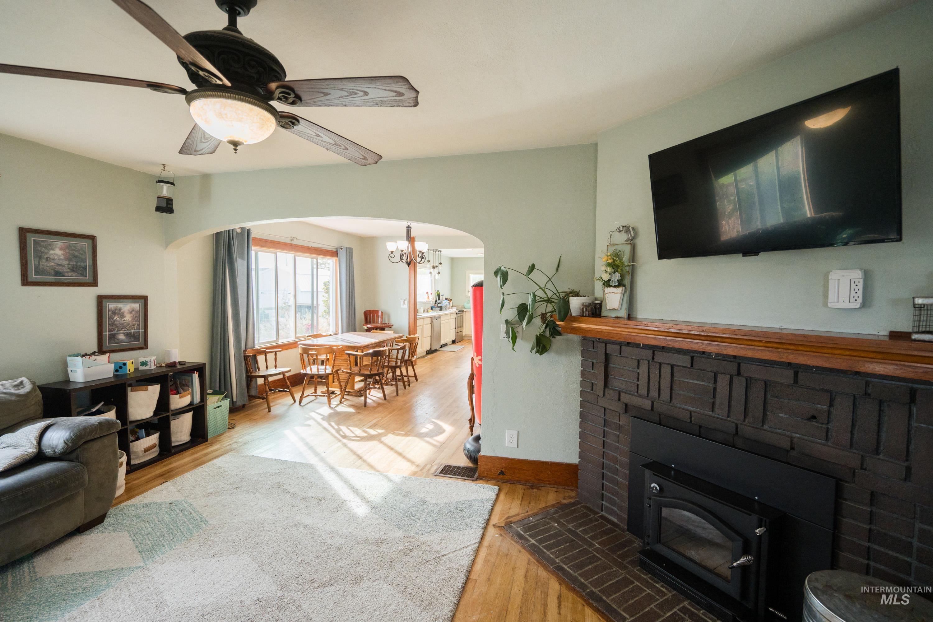 Living room with light wood-style floors, arched walkways, a chandelier, a ceiling fan, and a wood stove