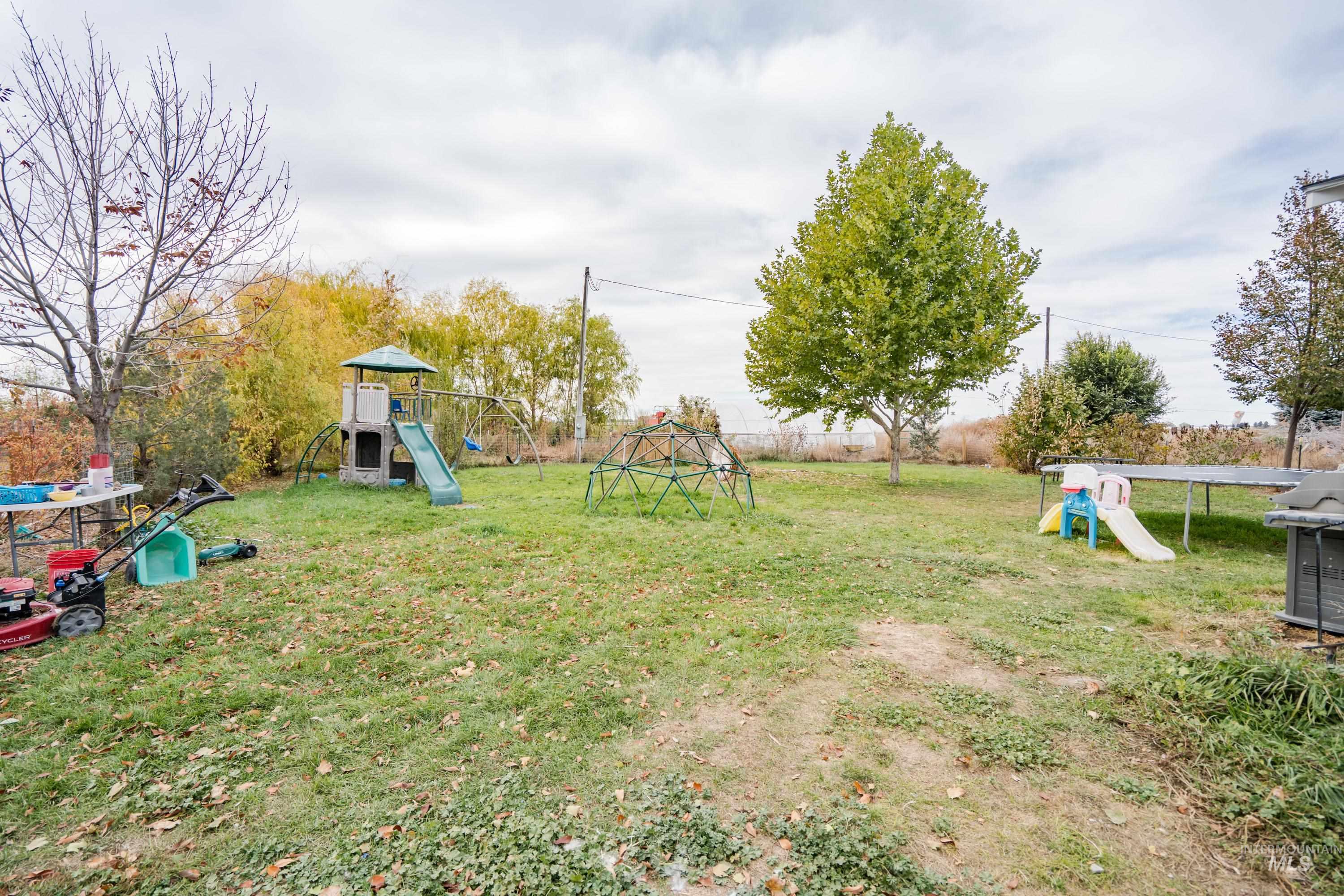 View of grassy yard featuring a playground and a trampoline
