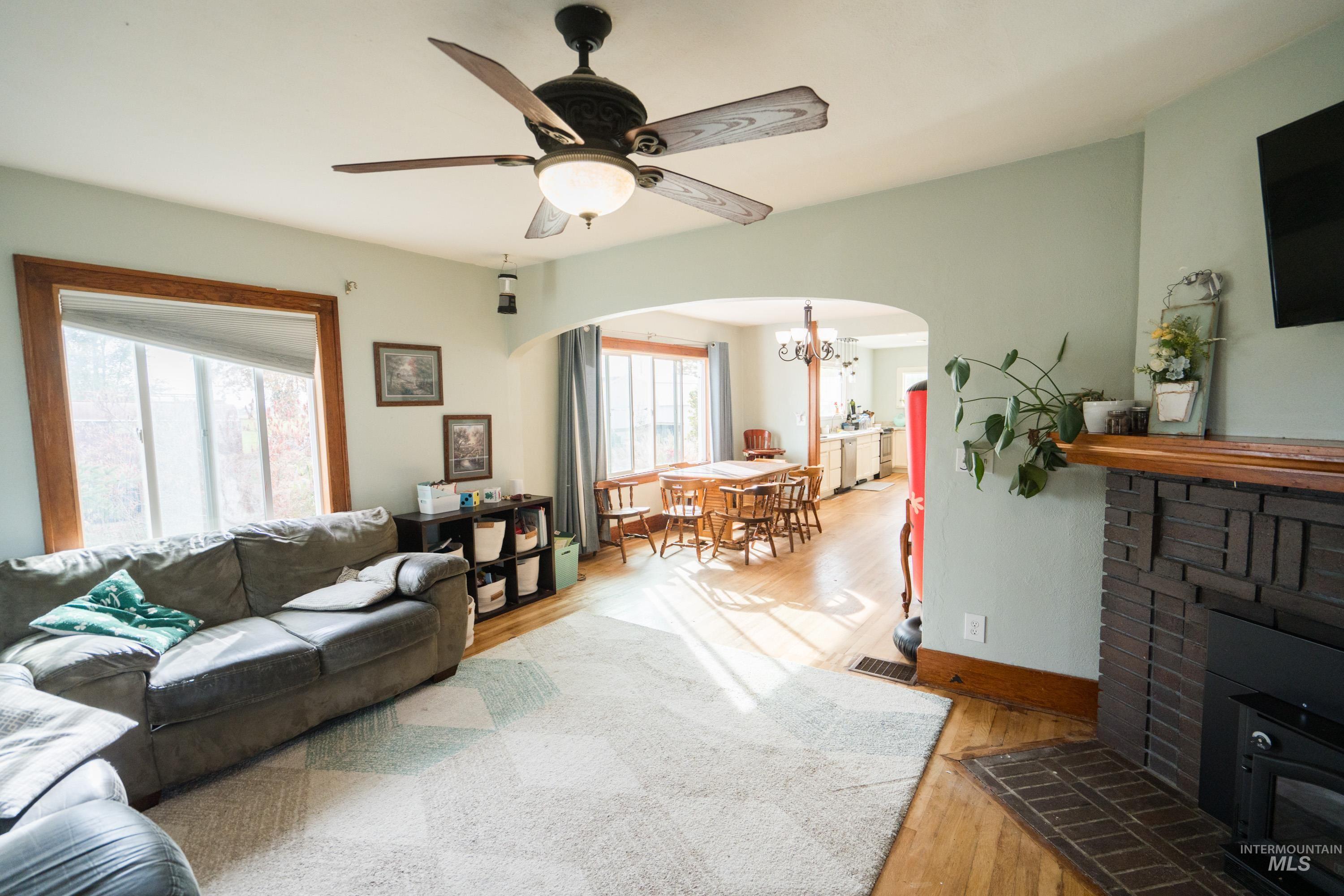Living area featuring light wood-style floors, ceiling fan, arched walkways, a chandelier, and a fireplace