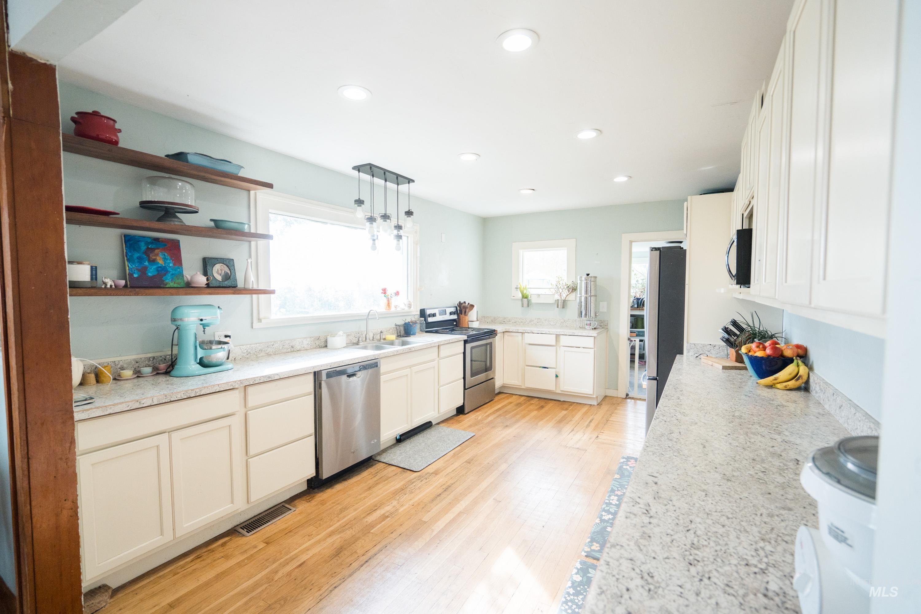 Kitchen with decorative light fixtures, appliances with stainless steel finishes, white cabinets, open shelves, and light wood-style floors