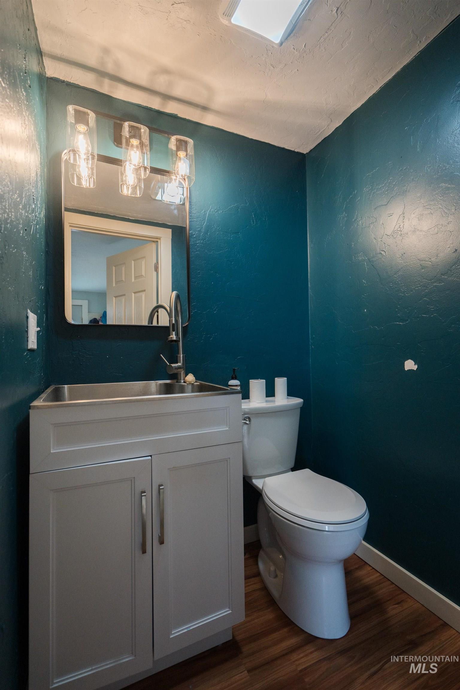 Half bathroom featuring a textured wall, dark wood finished floors, a textured ceiling, and vanity