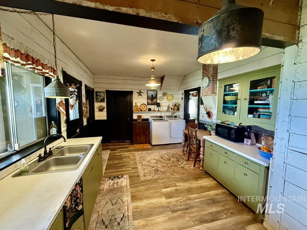 Kitchen with wood walls, green cabinetry, light wood finished floors, light countertops, and black microwave