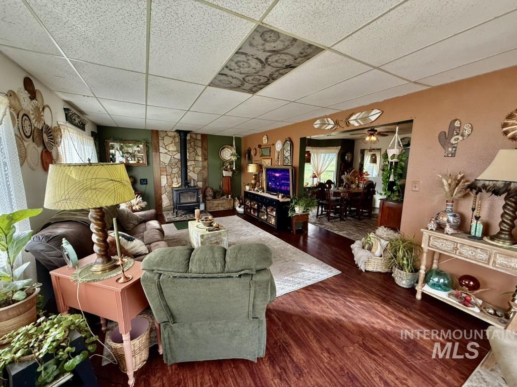 Living area featuring a wood stove, dark wood-type flooring, a paneled ceiling, and a ceiling fan