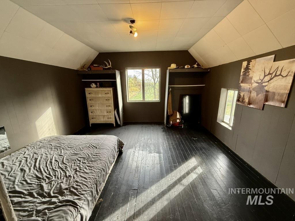 Bedroom with lofted ceiling, dark wood-style floors, and wooden walls