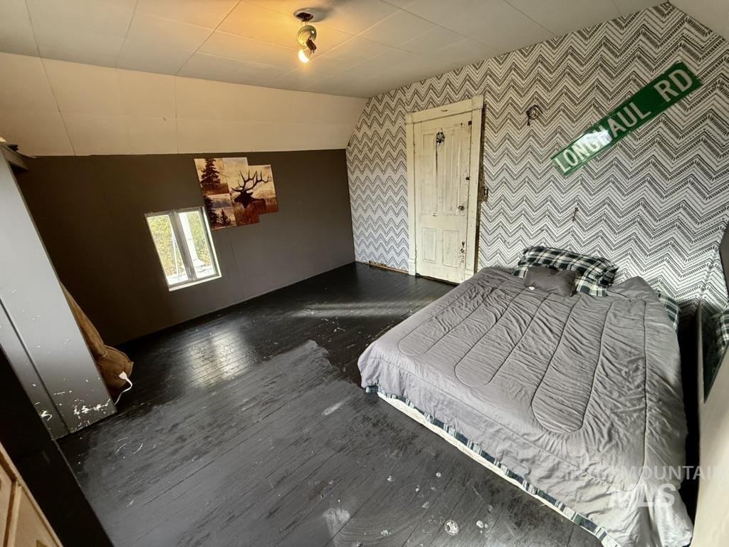 Bedroom with wood finished floors, lofted ceiling, and wallpapered walls