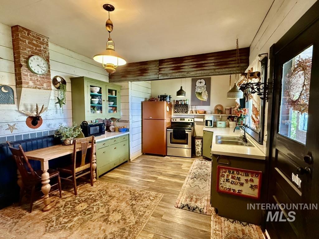 Kitchen with green cabinets, wooden walls, stainless steel range with electric stovetop, light countertops, and freestanding refrigerator