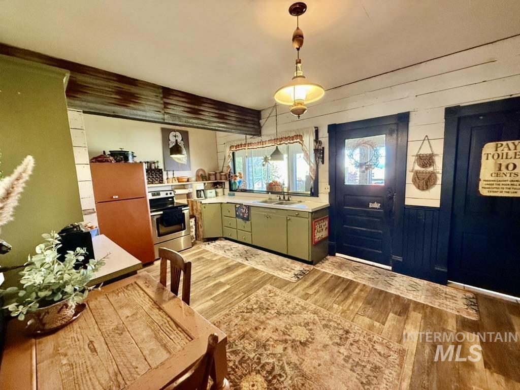 Kitchen featuring light countertops, light wood-type flooring, green cabinets, stainless steel range with electric cooktop, and pendant lighting