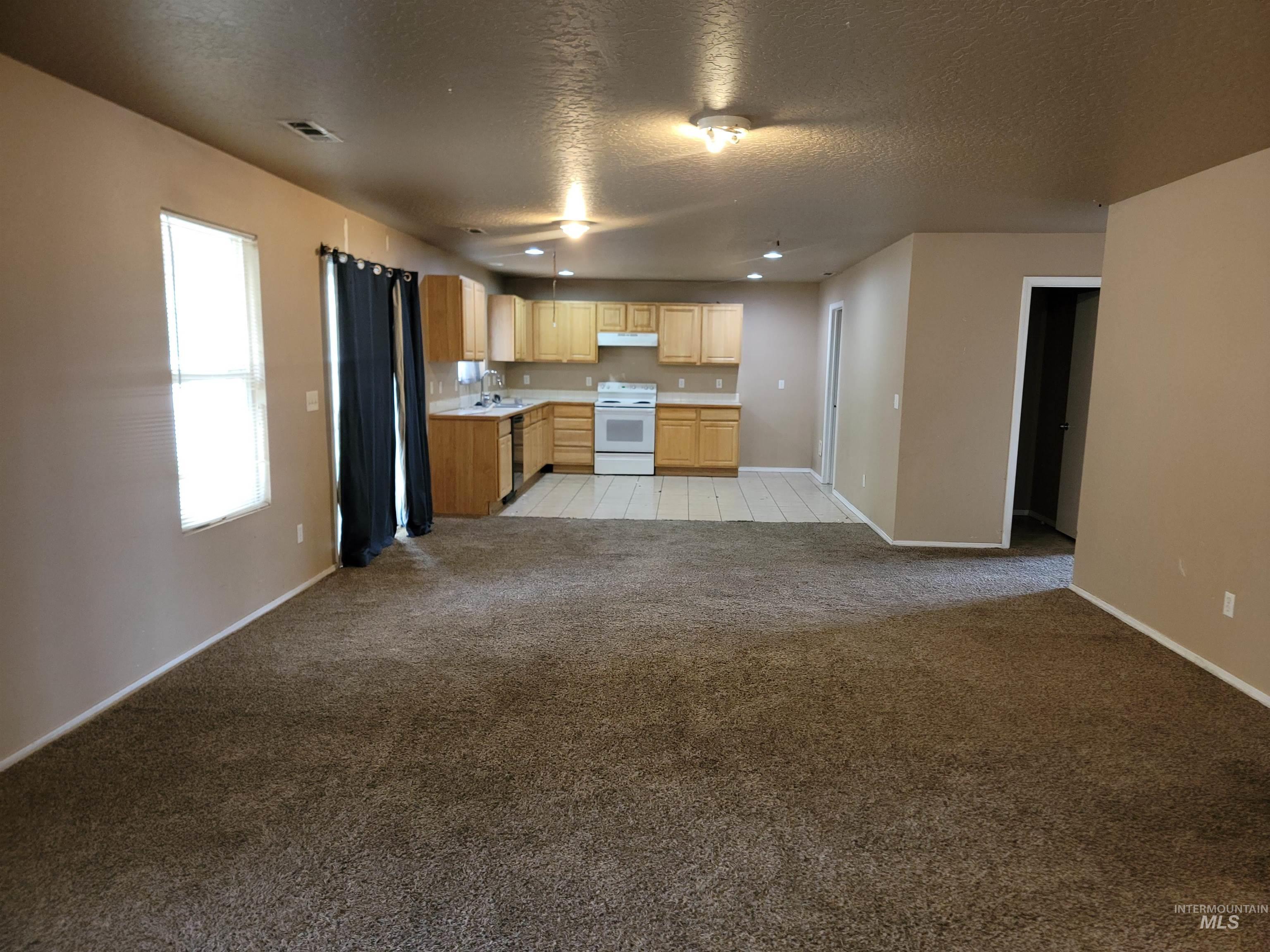 Kitchen featuring light brown cabinetry, light colored carpet, light countertops, a textured ceiling, and open floor plan