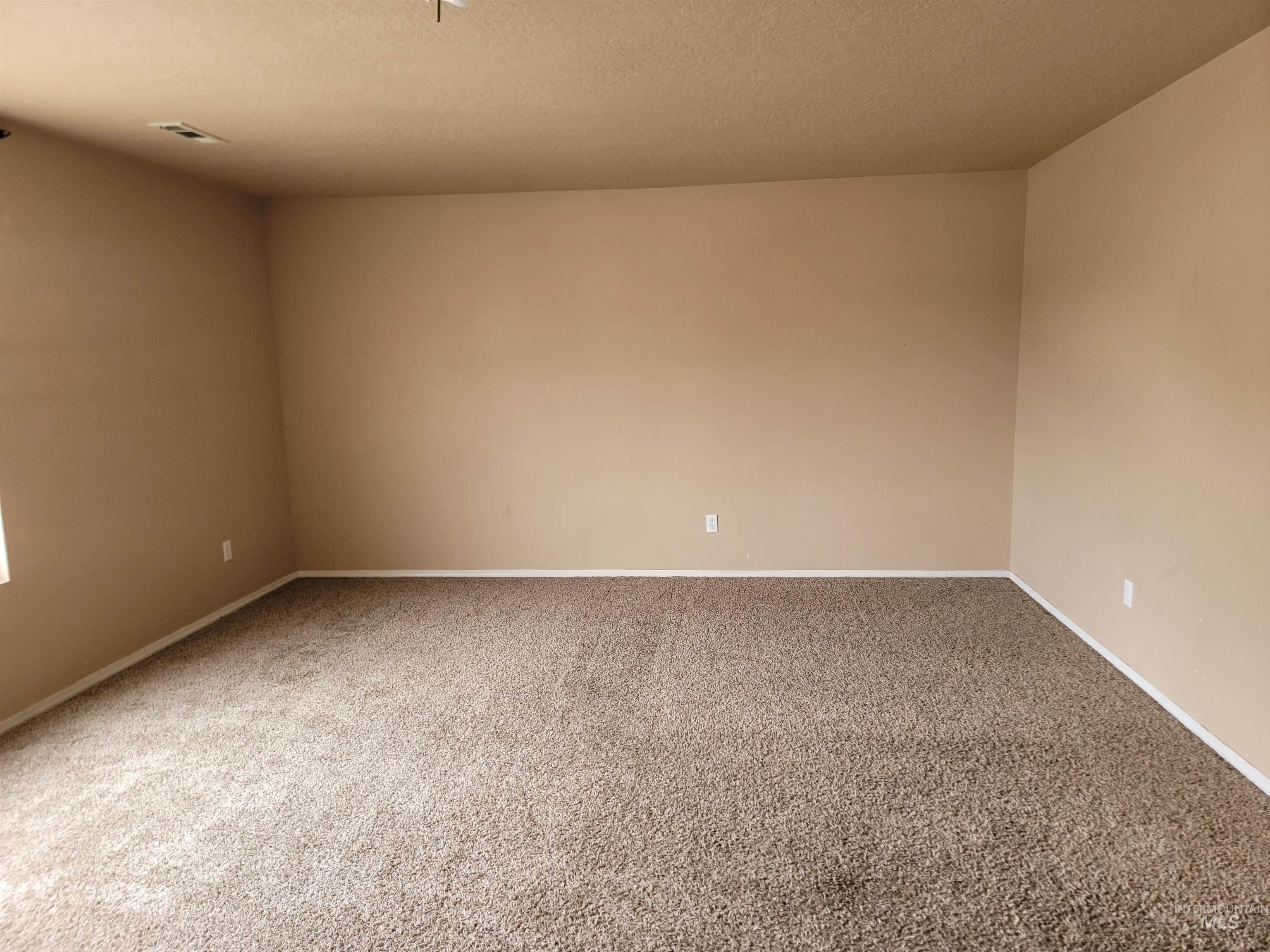 Carpeted spare room with a textured ceiling and baseboards