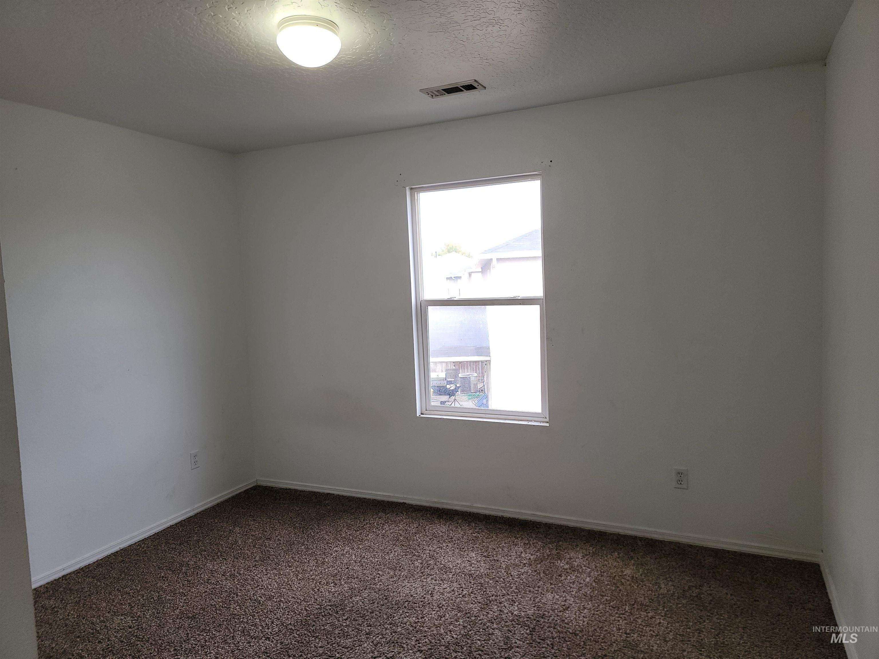 Empty room featuring dark carpet and a textured ceiling