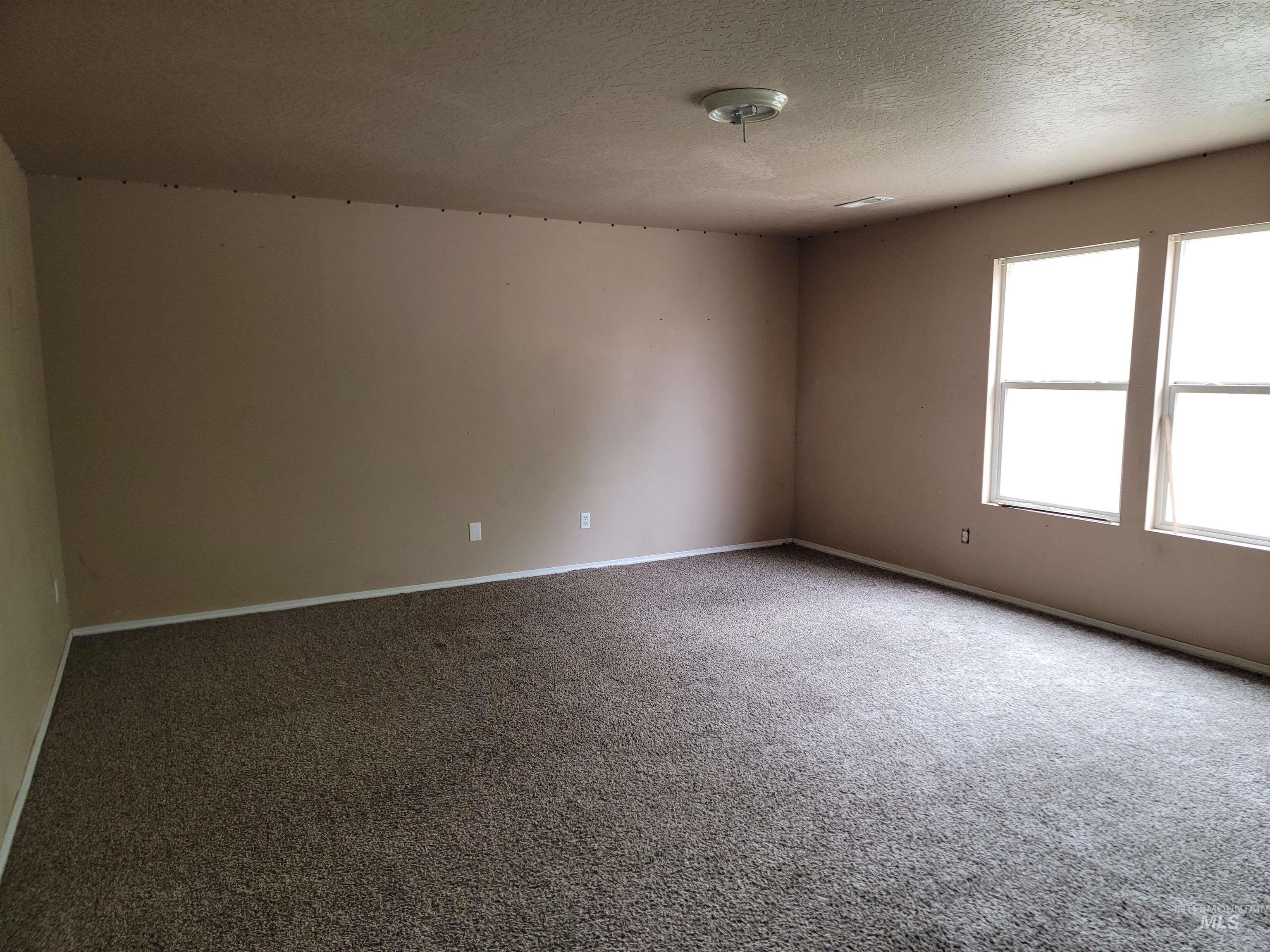 Carpeted empty room featuring a textured ceiling and baseboards