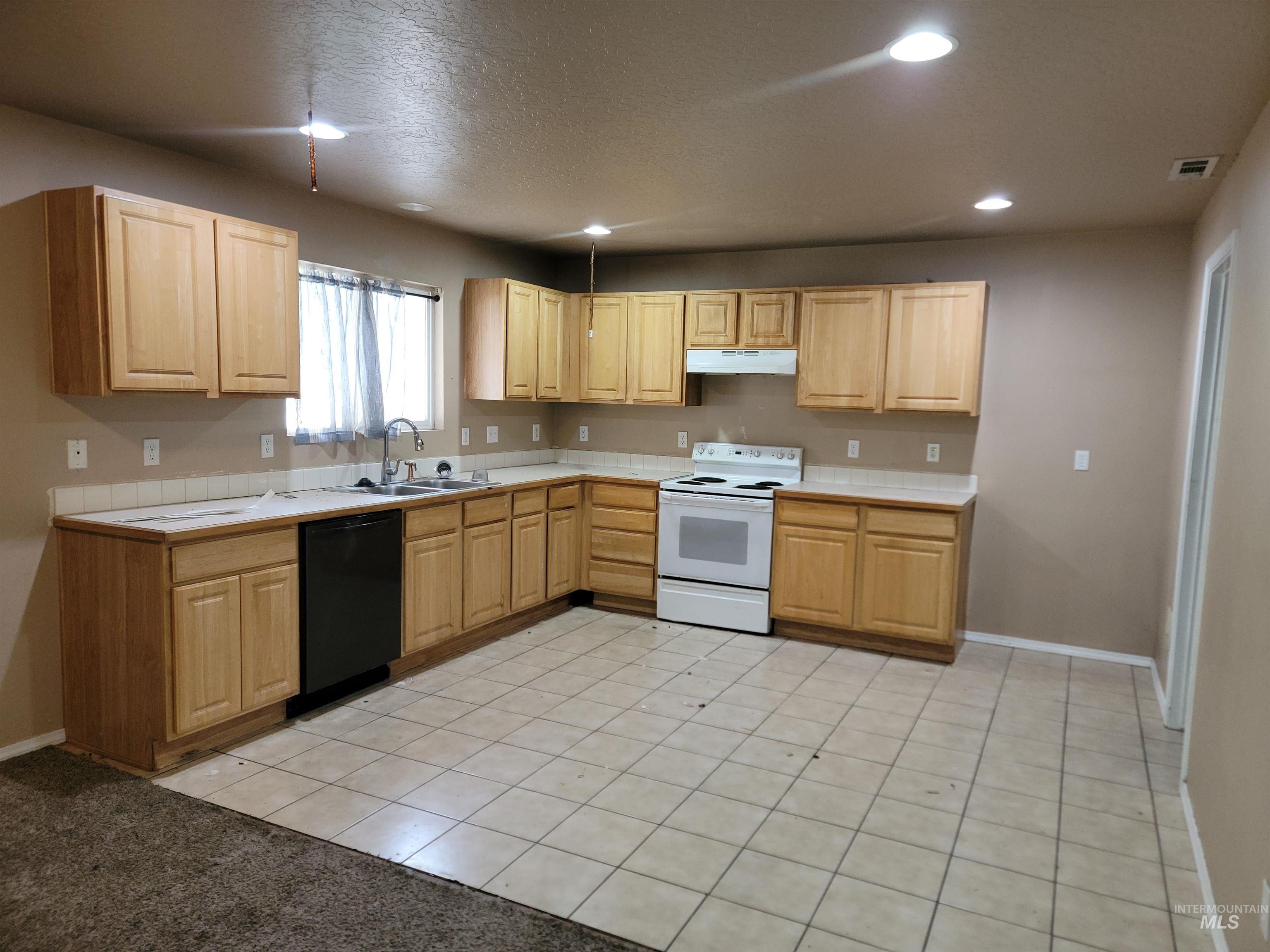 Kitchen featuring light tile patterned floors, white range with electric cooktop, black dishwasher, light brown cabinets, and recessed lighting