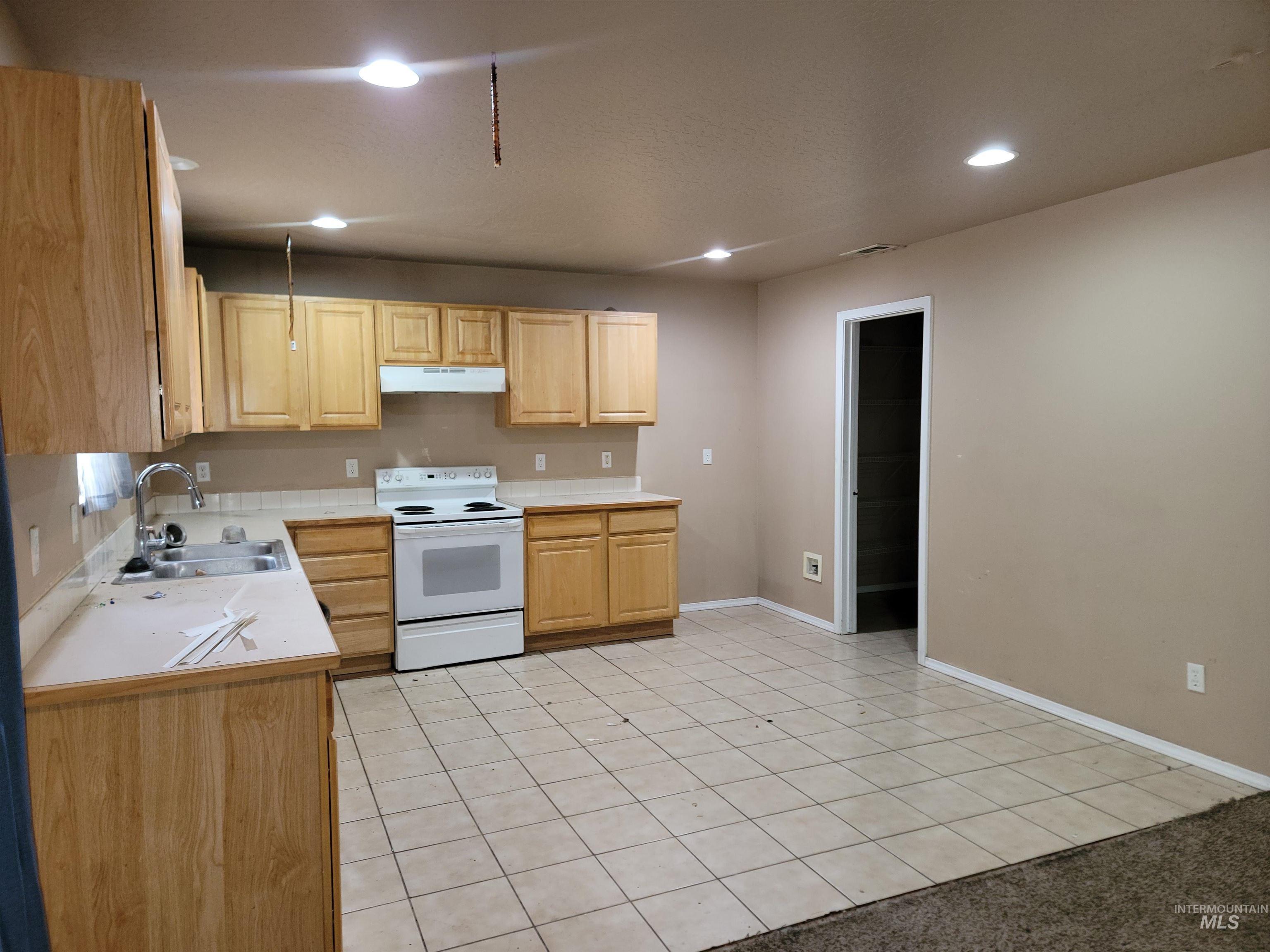 Kitchen with light tile patterned floors, light countertops, electric stove, recessed lighting, and light brown cabinetry