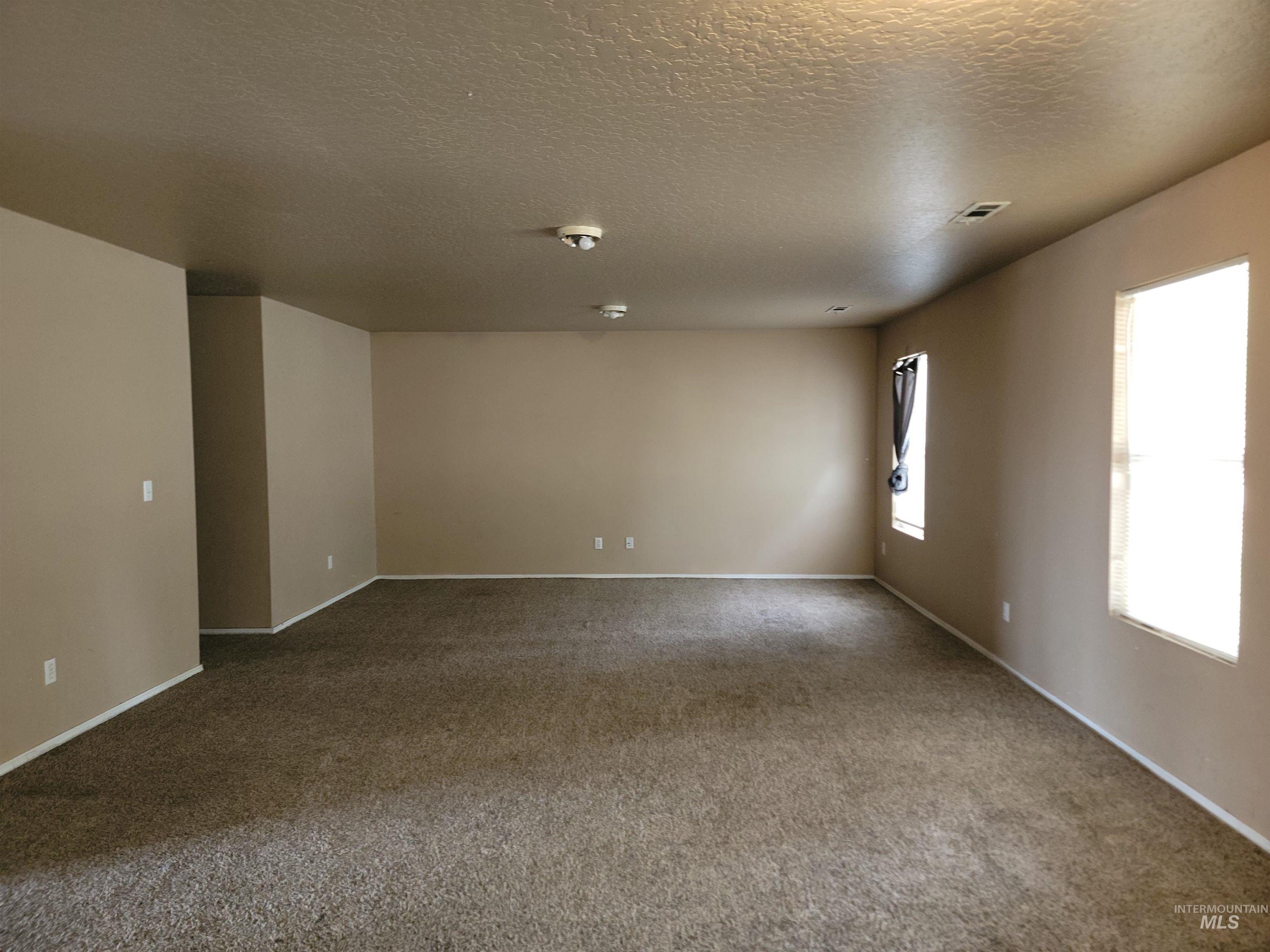 Empty room with dark colored carpet and a textured ceiling