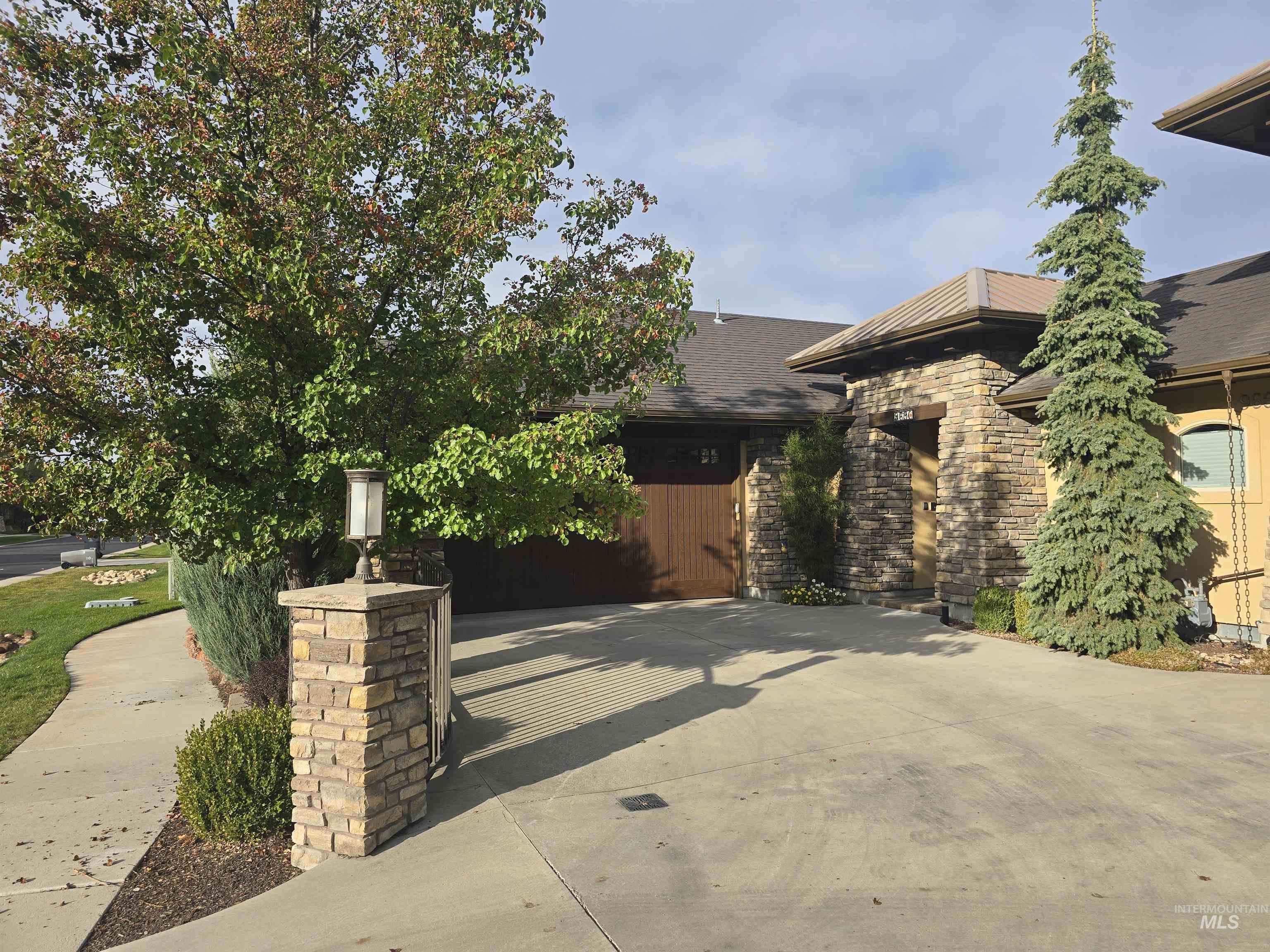 View of front facade with concrete driveway, roof with shingles, and stone siding