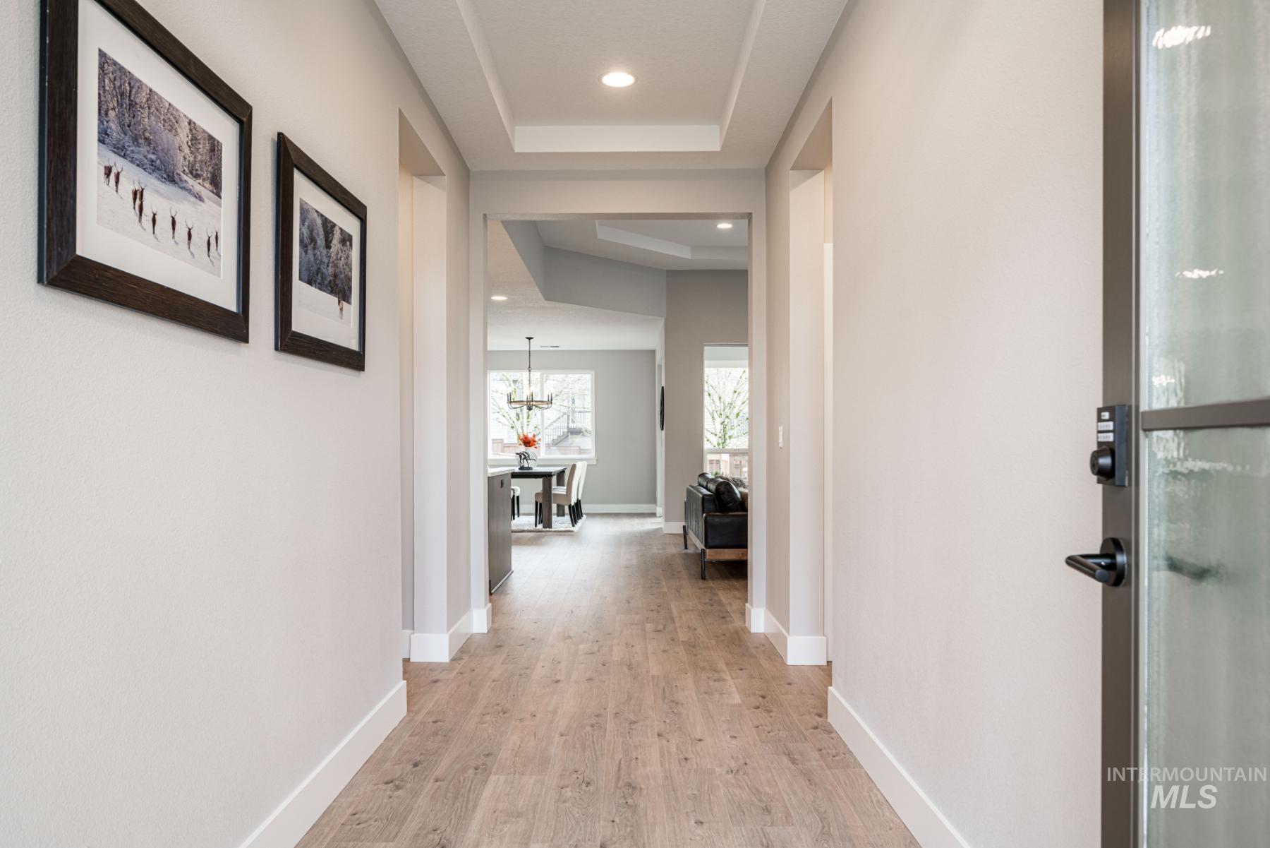 Hall with a raised ceiling, light wood-style floors, recessed lighting, and a chandelier