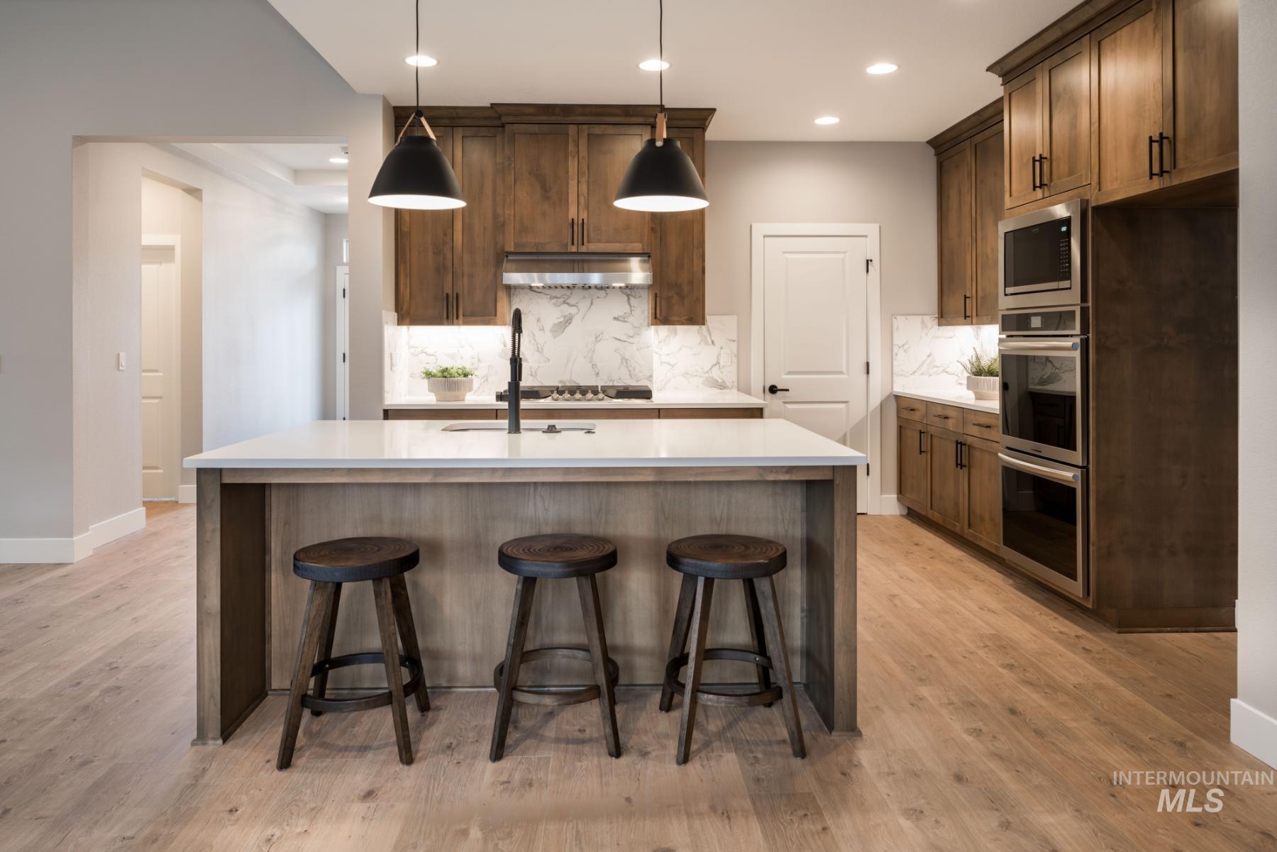 Kitchen with decorative backsplash, appliances with stainless steel finishes, an island with sink, light wood-style floors, and light countertops