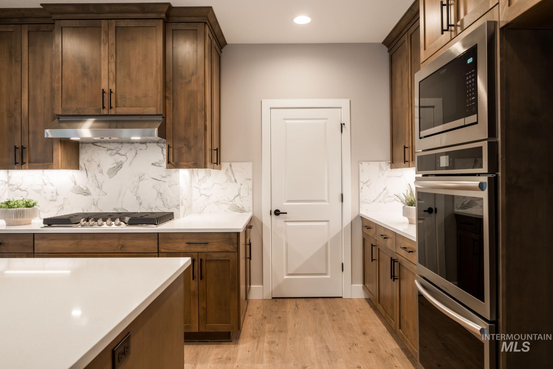 Kitchen featuring appliances with stainless steel finishes, light wood-style floors, light countertops, tasteful backsplash, and ventilation hood