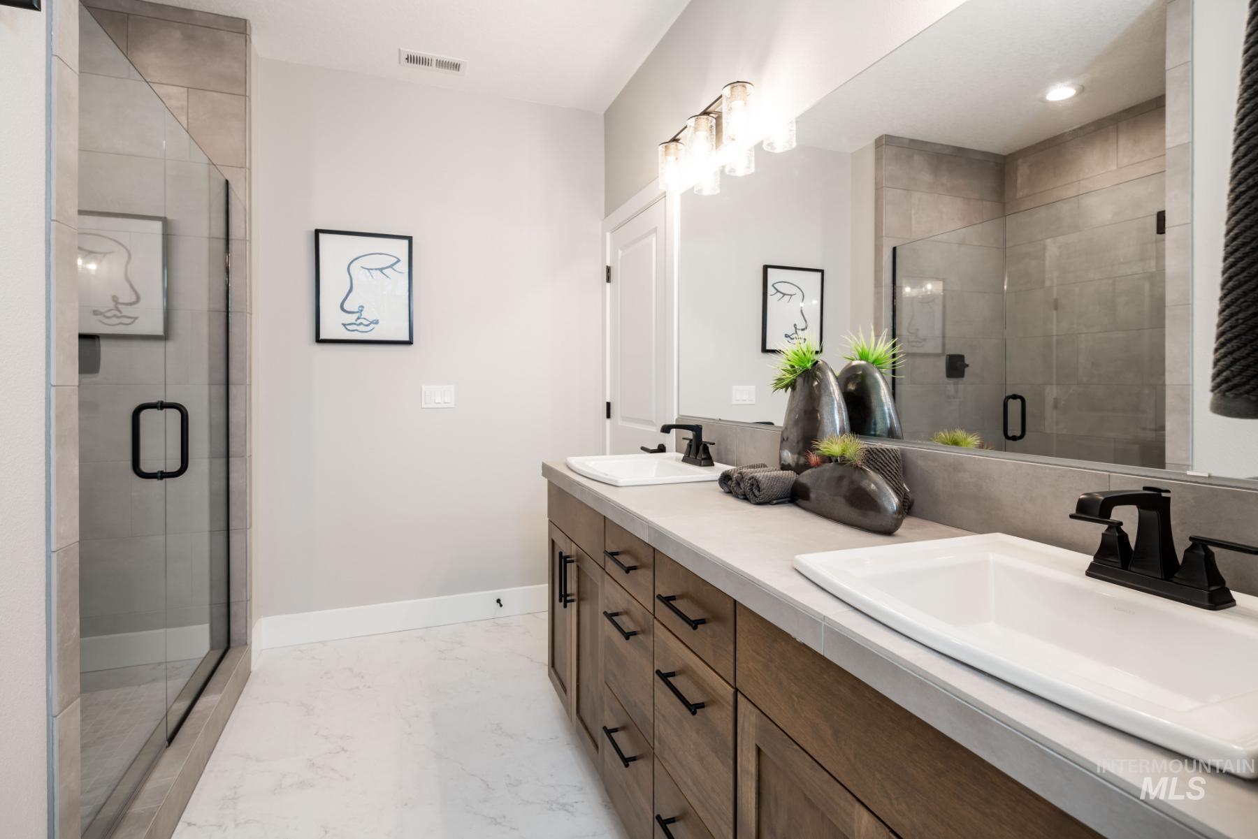 Full bath featuring double vanity, a stall shower, and marble finish floors