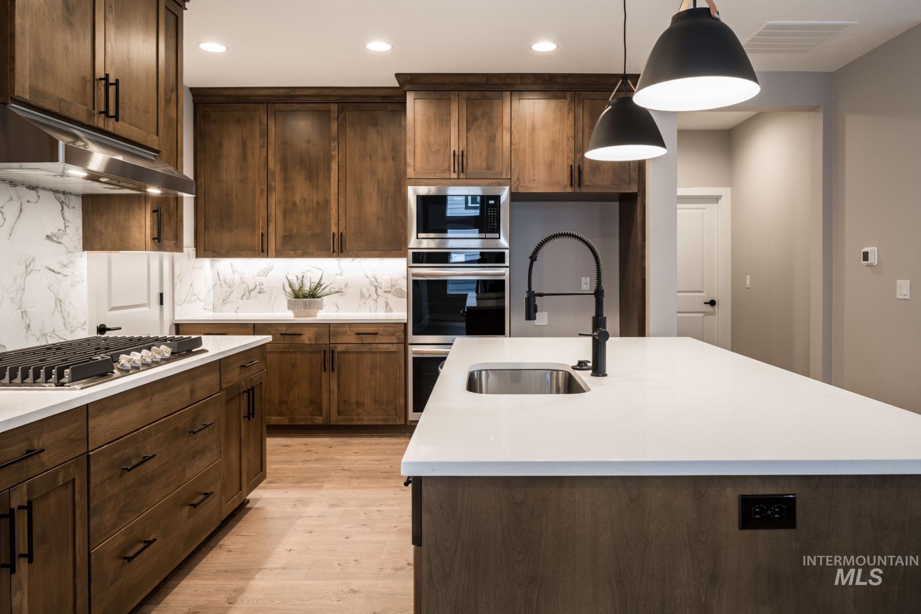 Kitchen featuring light countertops, backsplash, recessed lighting, an island with sink, and light wood finished floors