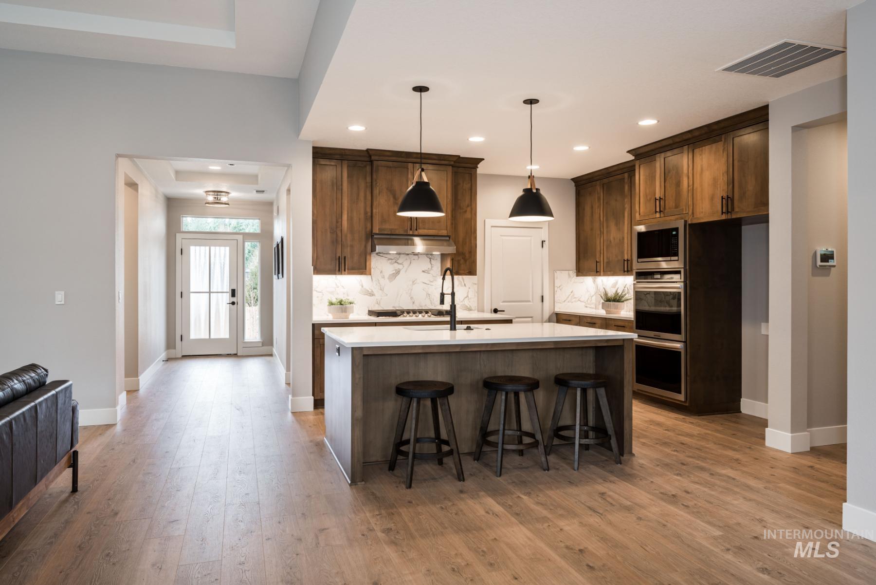 Kitchen with backsplash, light countertops, a kitchen island with sink, light wood finished floors, and recessed lighting