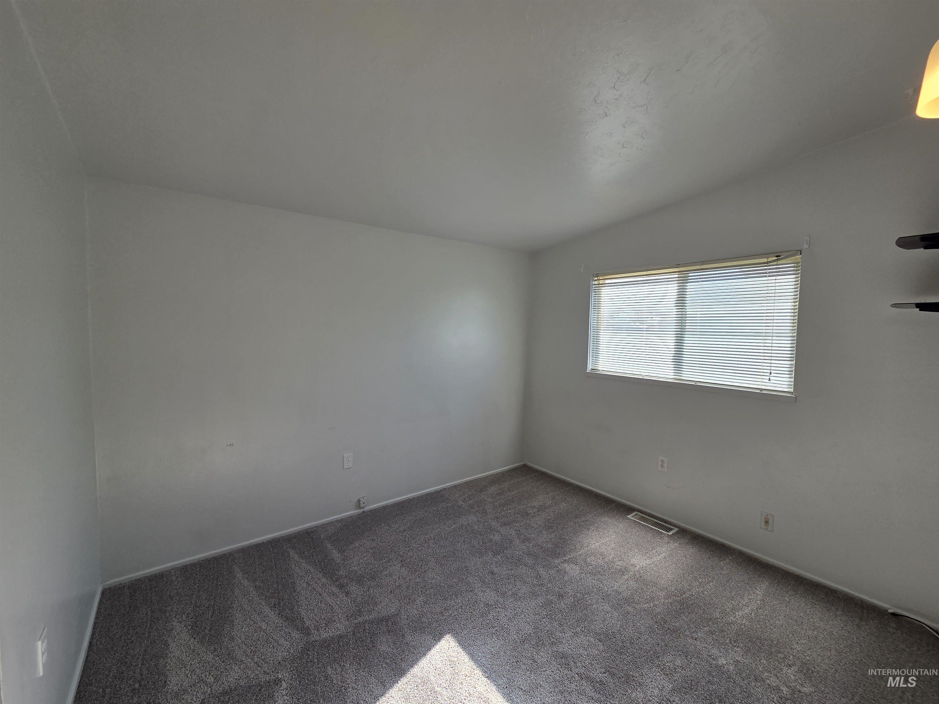 Carpeted spare room with vaulted ceiling and baseboards