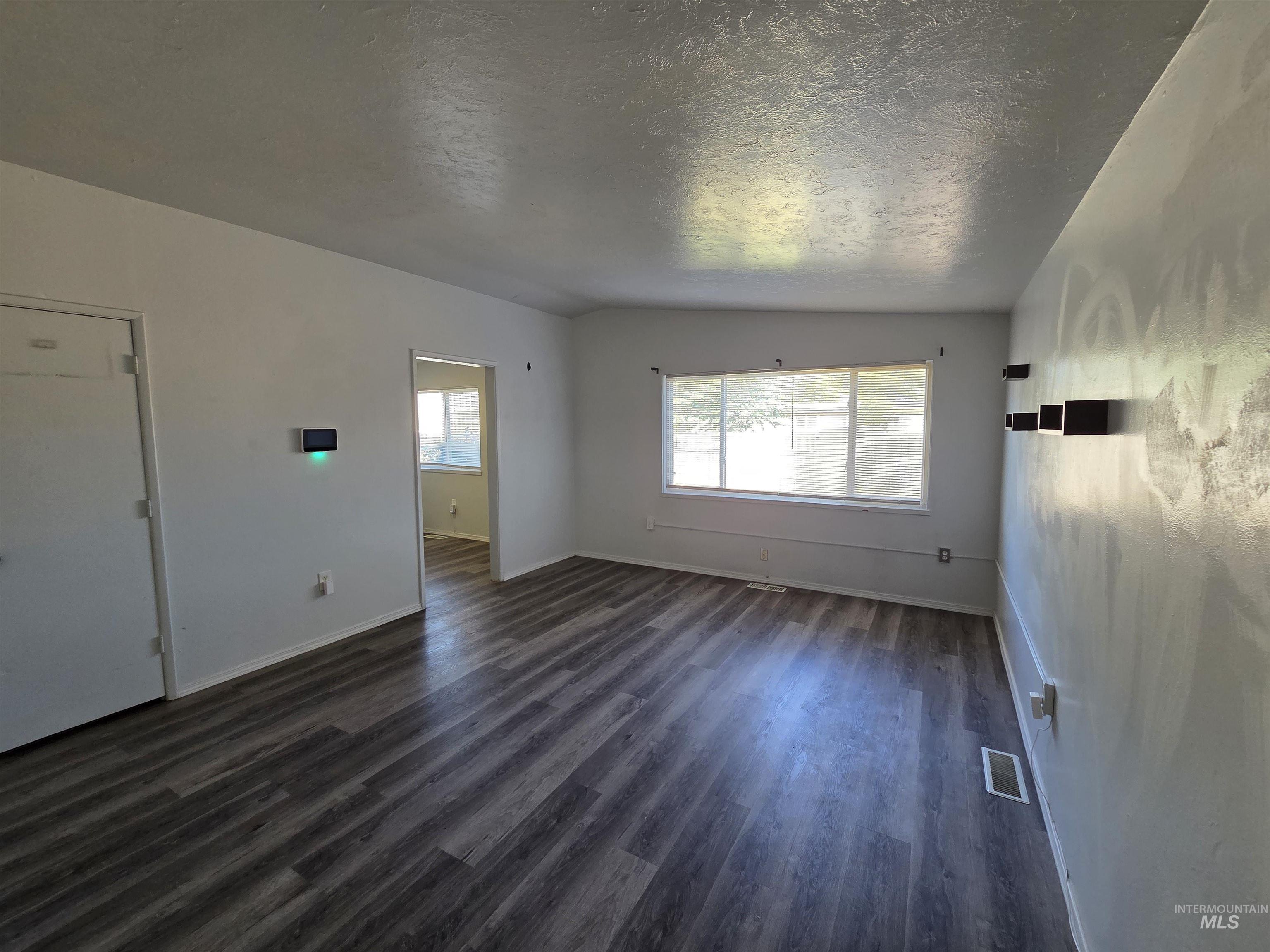 Unfurnished living room featuring dark wood-style flooring and a textured ceiling