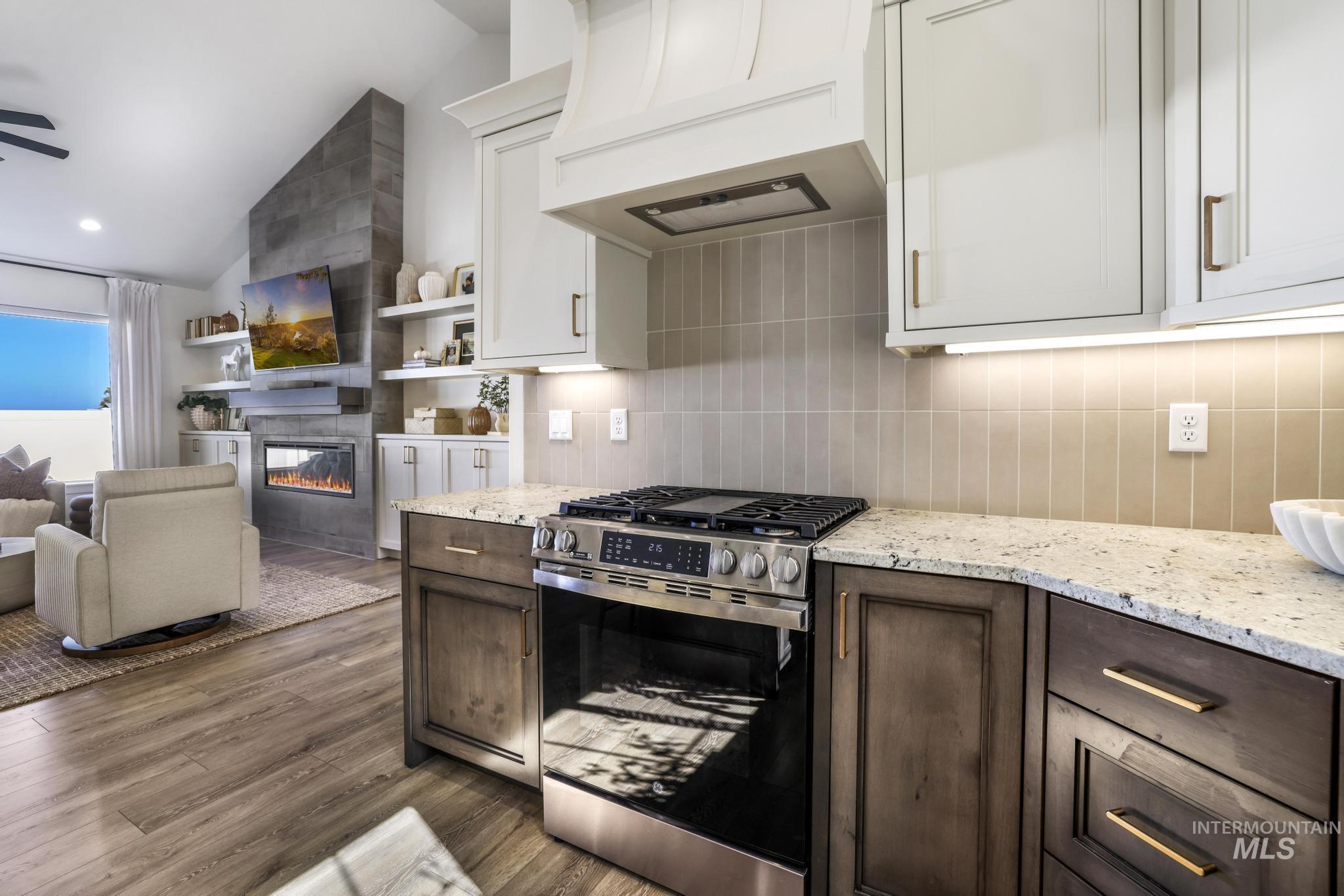Kitchen with stainless steel range with gas stovetop, dark brown cabinetry, white cabinets, custom exhaust hood, and vaulted ceiling