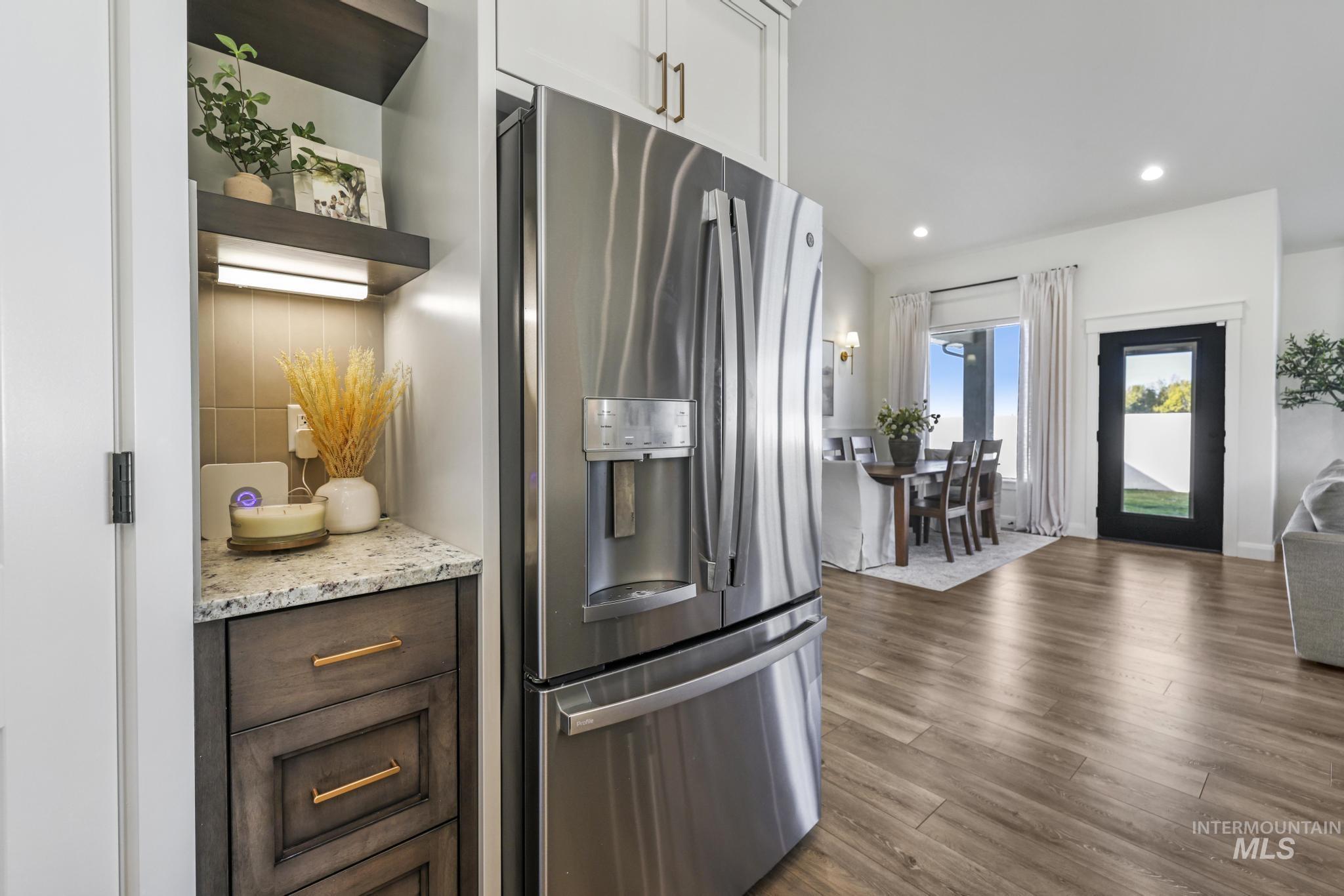 Kitchen with stainless steel refrigerator with ice dispenser, light stone countertops, dark wood-style flooring, dark brown cabinets, and open shelves