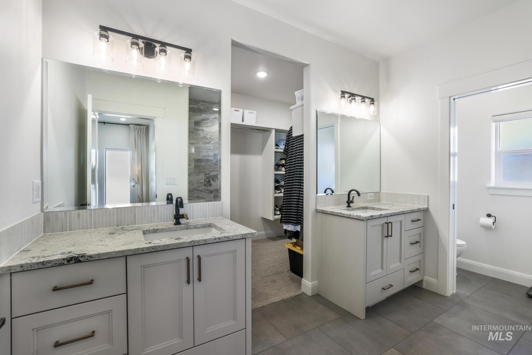 Bathroom with two vanities, a walk in closet, and dark tile patterned flooring
