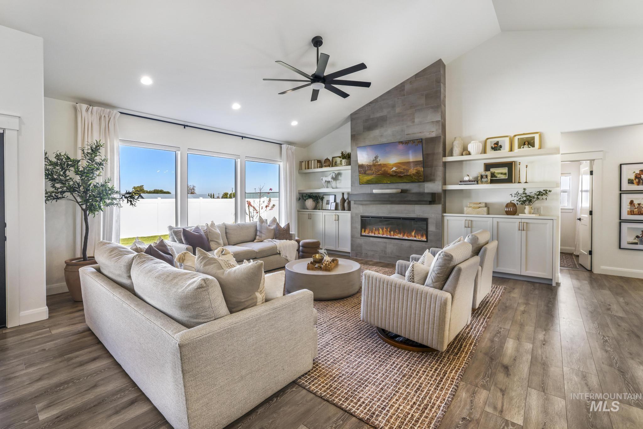 Living room featuring high vaulted ceiling, healthy amount of natural light, a tiled fireplace, dark wood-type flooring, and a ceiling fan
