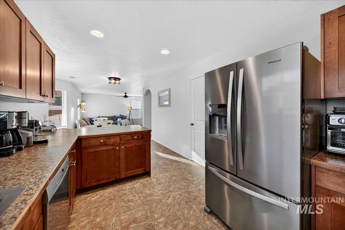 Kitchen featuring stainless steel appliances, brown cabinetry, open floor plan, dark countertops, and a textured ceiling