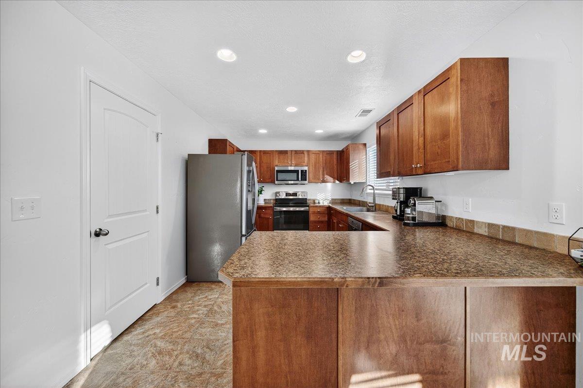 Kitchen with appliances with stainless steel finishes, brown cabinetry, recessed lighting, a peninsula, and dark countertops