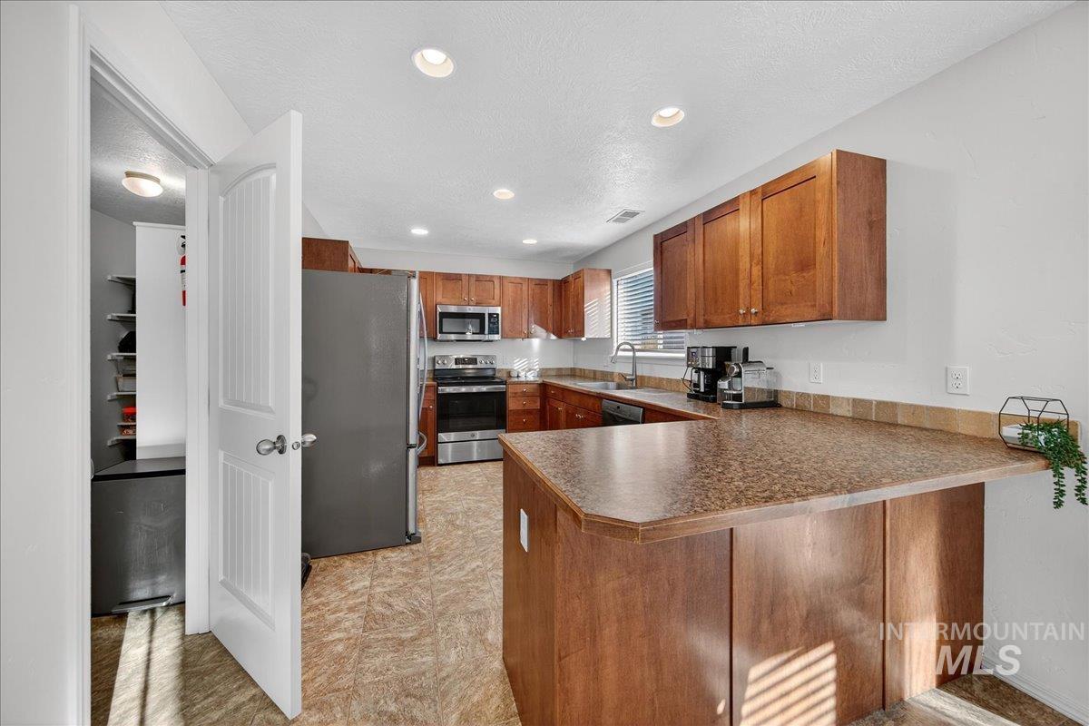 Kitchen featuring brown cabinetry, appliances with stainless steel finishes, dark countertops, recessed lighting, and a peninsula