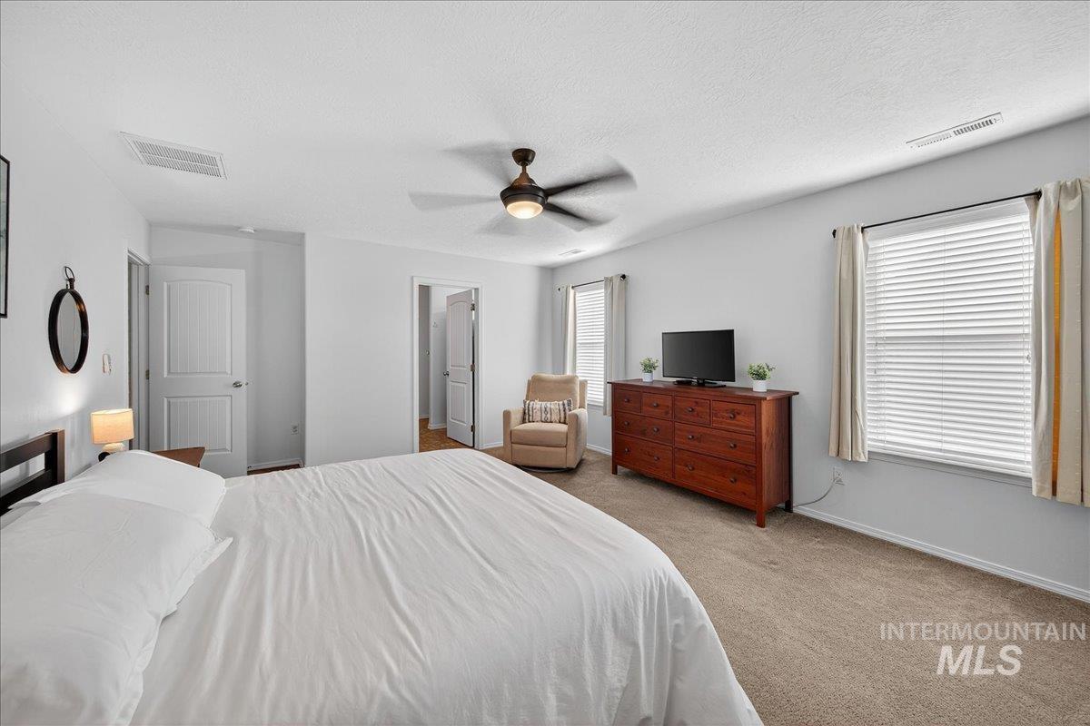 Bedroom with light colored carpet, multiple windows, a ceiling fan, and a textured ceiling