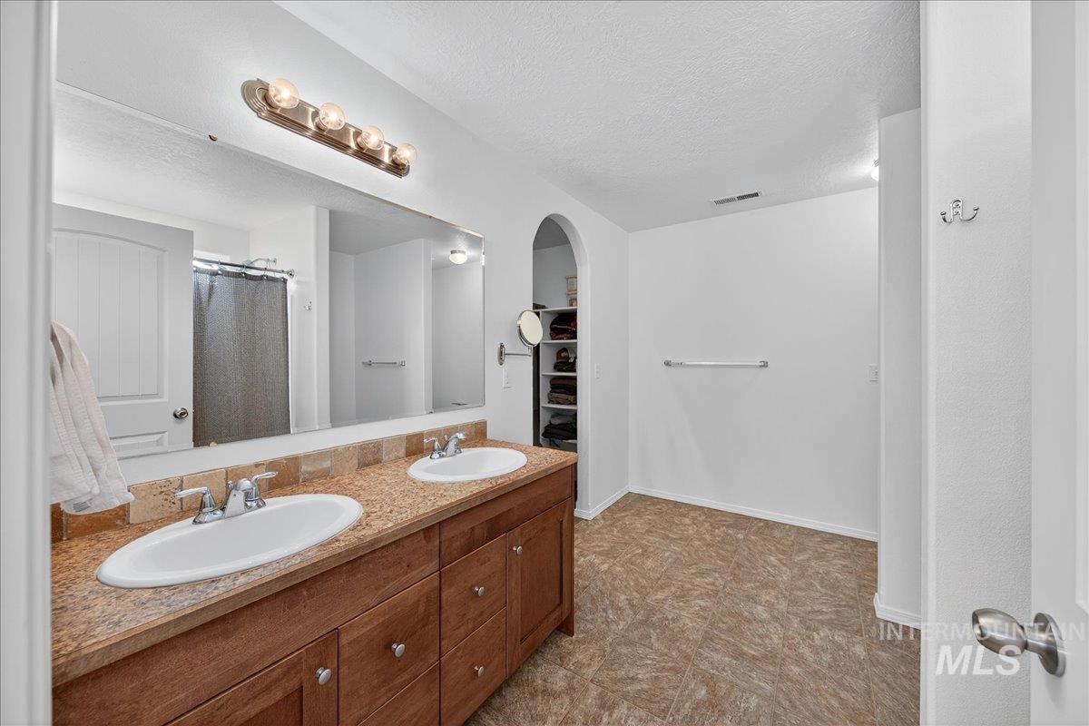 Full bath with double vanity, a textured ceiling, a walk in closet, and a shower with shower curtain