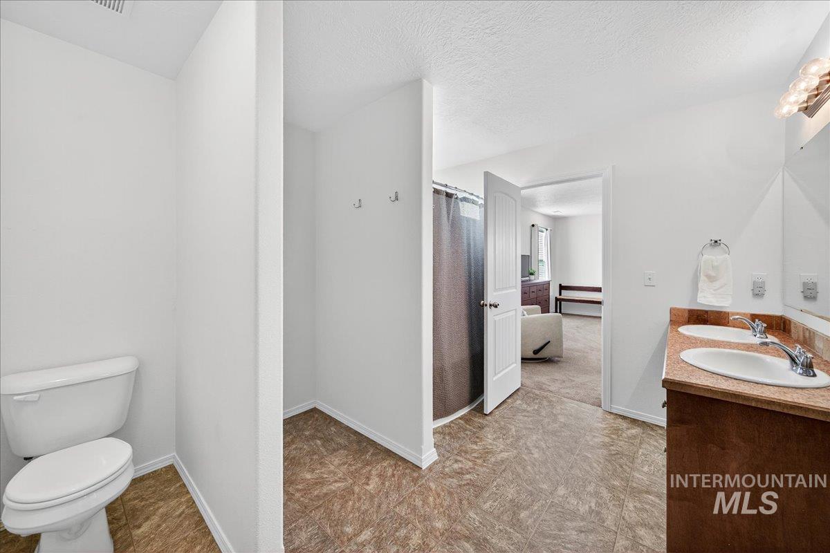 Ensuite bathroom featuring double vanity, curtained shower, and a textured ceiling