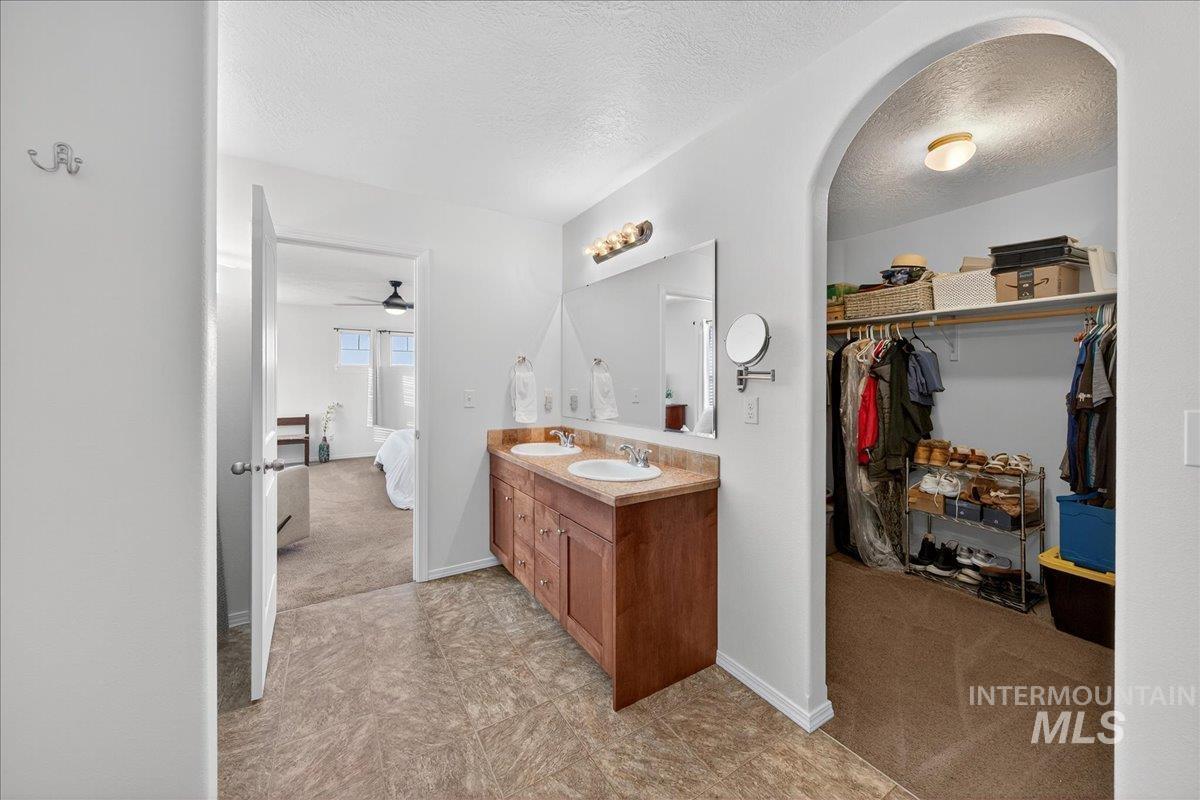 Ensuite bathroom featuring a textured ceiling, double vanity, a walk in closet, light colored carpet, and ceiling fan