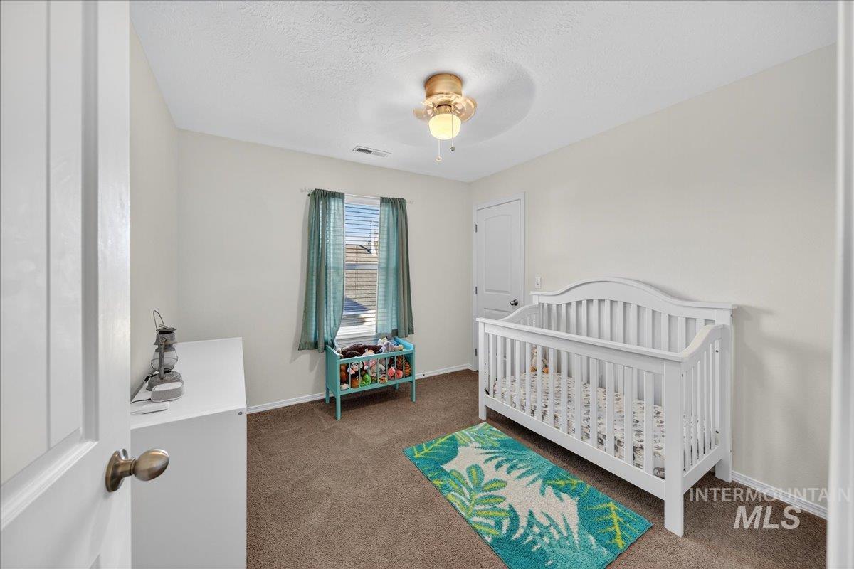 Bedroom featuring a nursery area, dark colored carpet, a textured ceiling, and ceiling fan