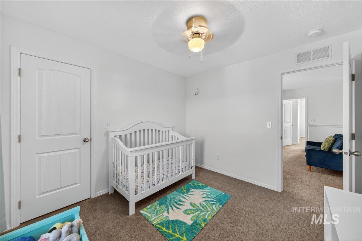 Carpeted bedroom with a crib, ceiling fan, and a textured ceiling