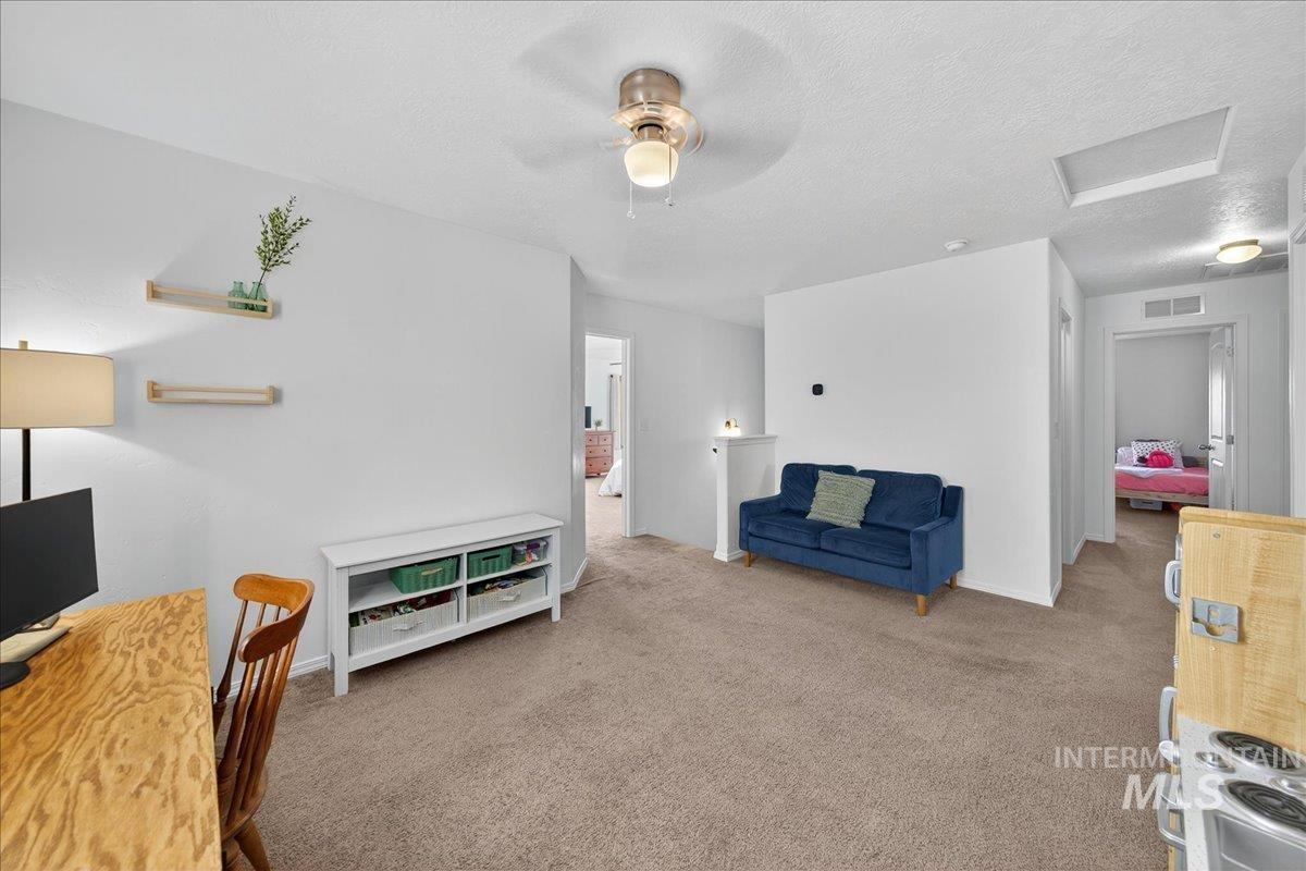 Living area with carpet flooring, attic access, a textured ceiling, a desk, and ceiling fan