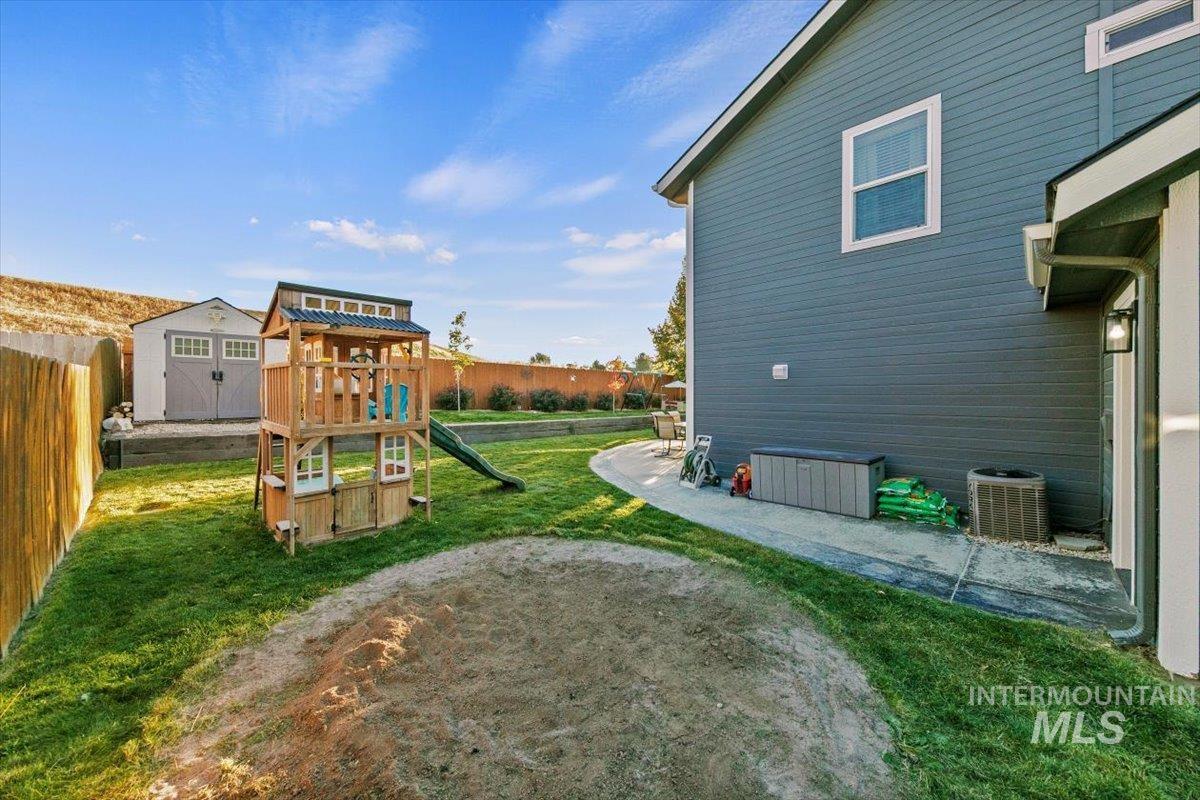 Fenced backyard featuring a playground, a shed, and a patio