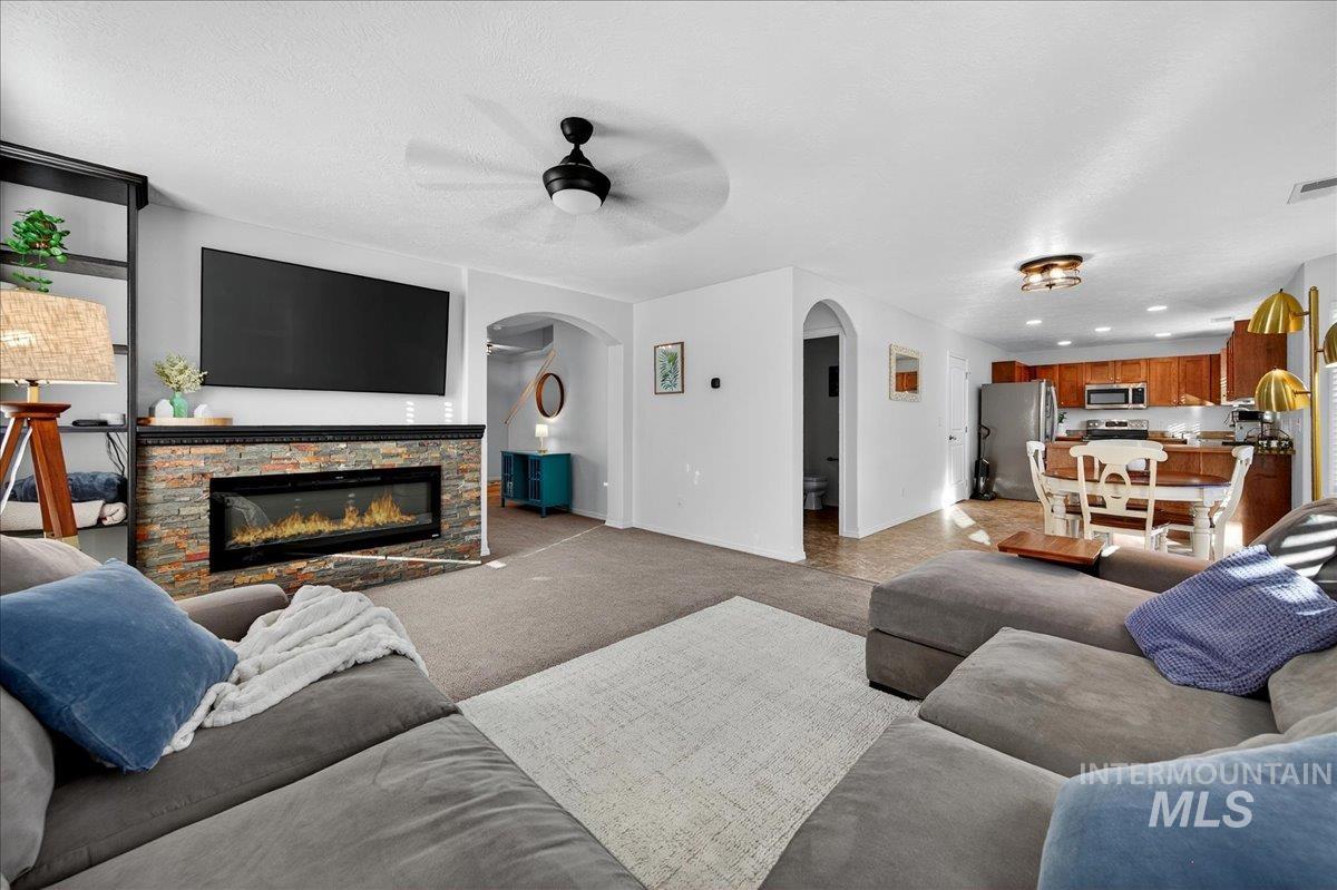Living area featuring light colored carpet, a stone fireplace, a ceiling fan, and recessed lighting